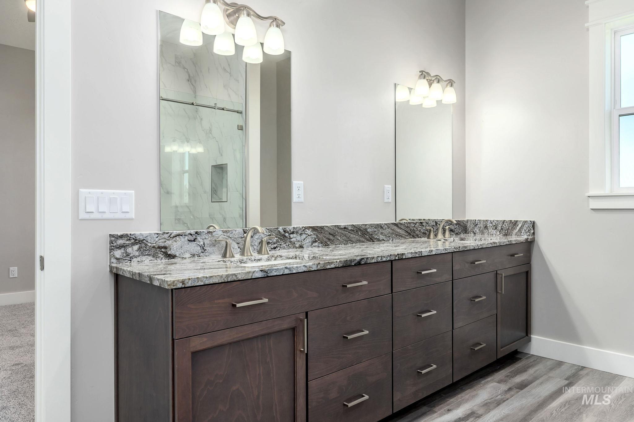Full bath with double vanity, a marble finish shower, and wood finished floors