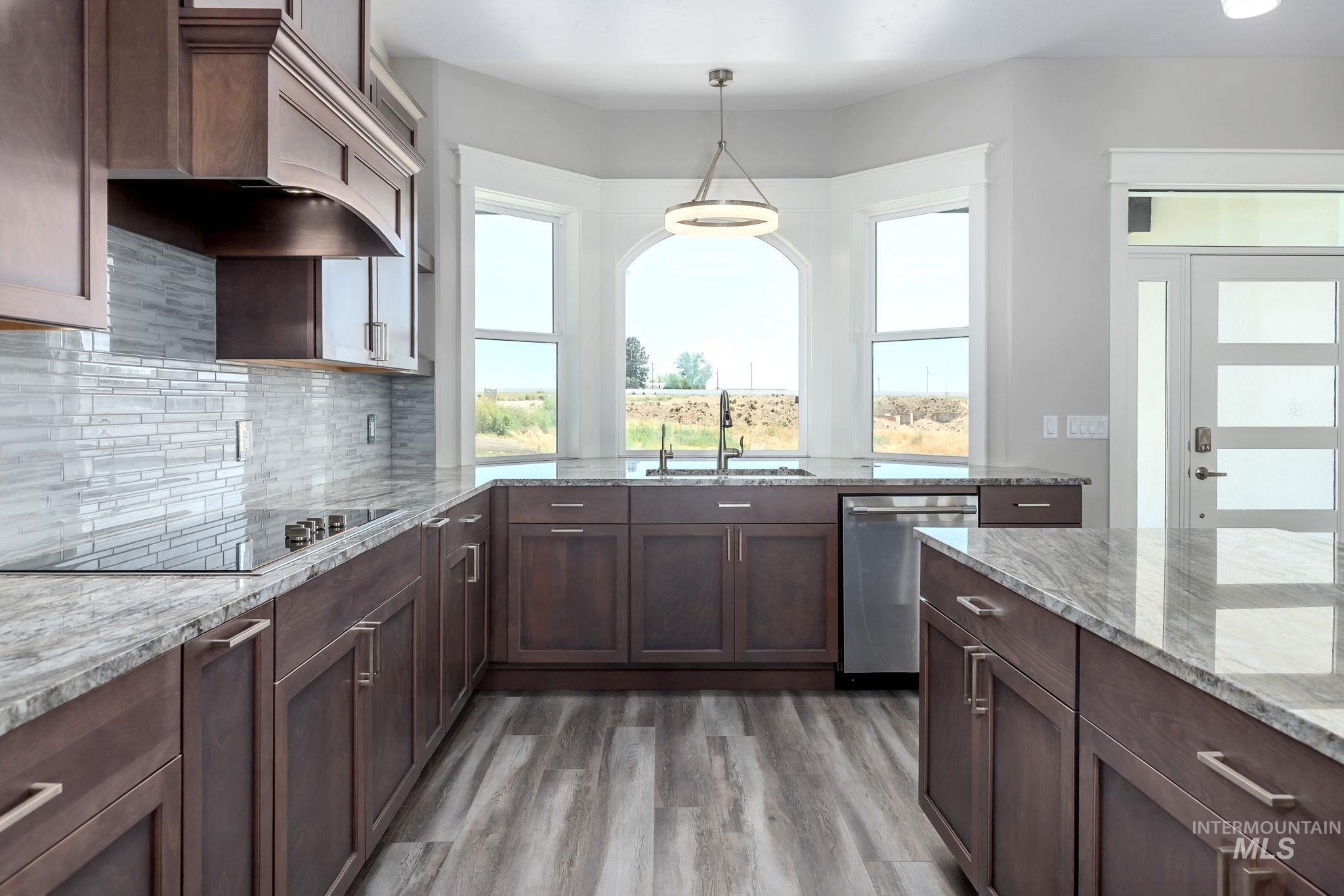 Kitchen with custom range hood, dishwasher, light wood-style floors, backsplash, and pendant lighting