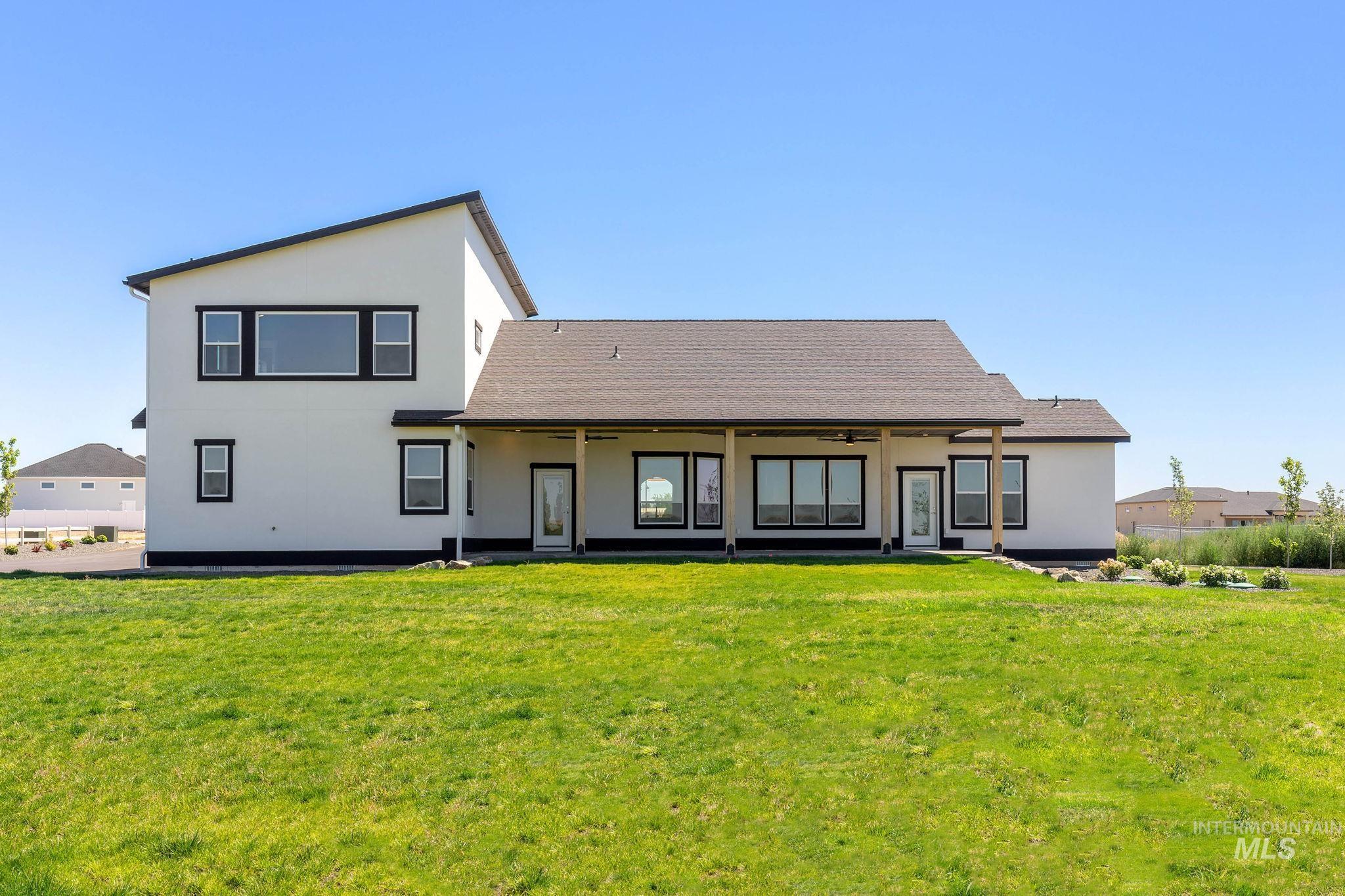 Back of property with ceiling fan, stucco siding, a lawn, and roof with shingles