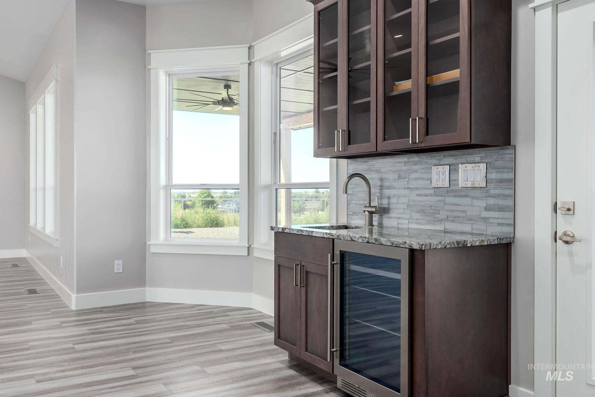 Indoor wet bar with beverage cooler, tasteful backsplash, light wood-style flooring, and a ceiling fan