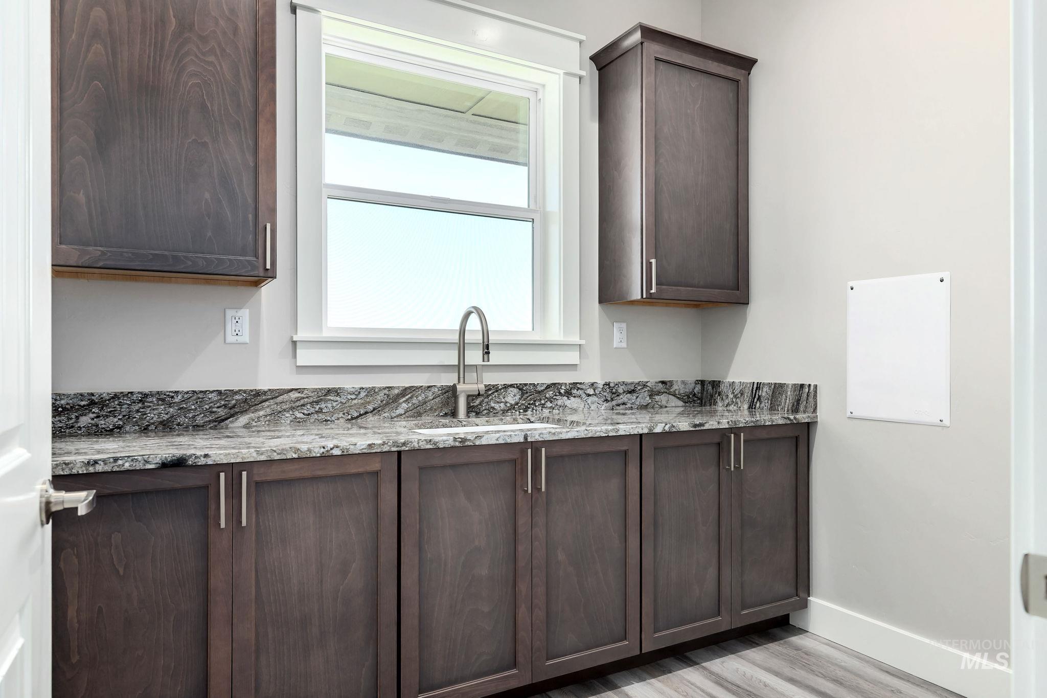 Laundry with dark brown cabinets, light wood-type flooring, and light stone counters