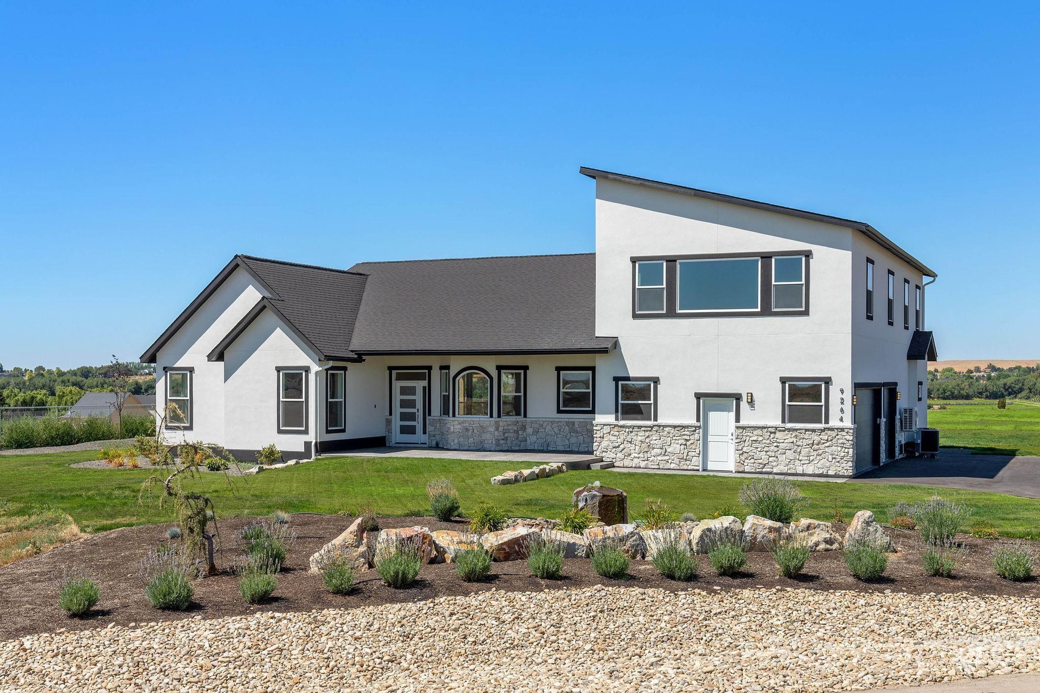 View of front of house with an attached garage, stucco siding, a front yard, a shingled roof, and stone siding