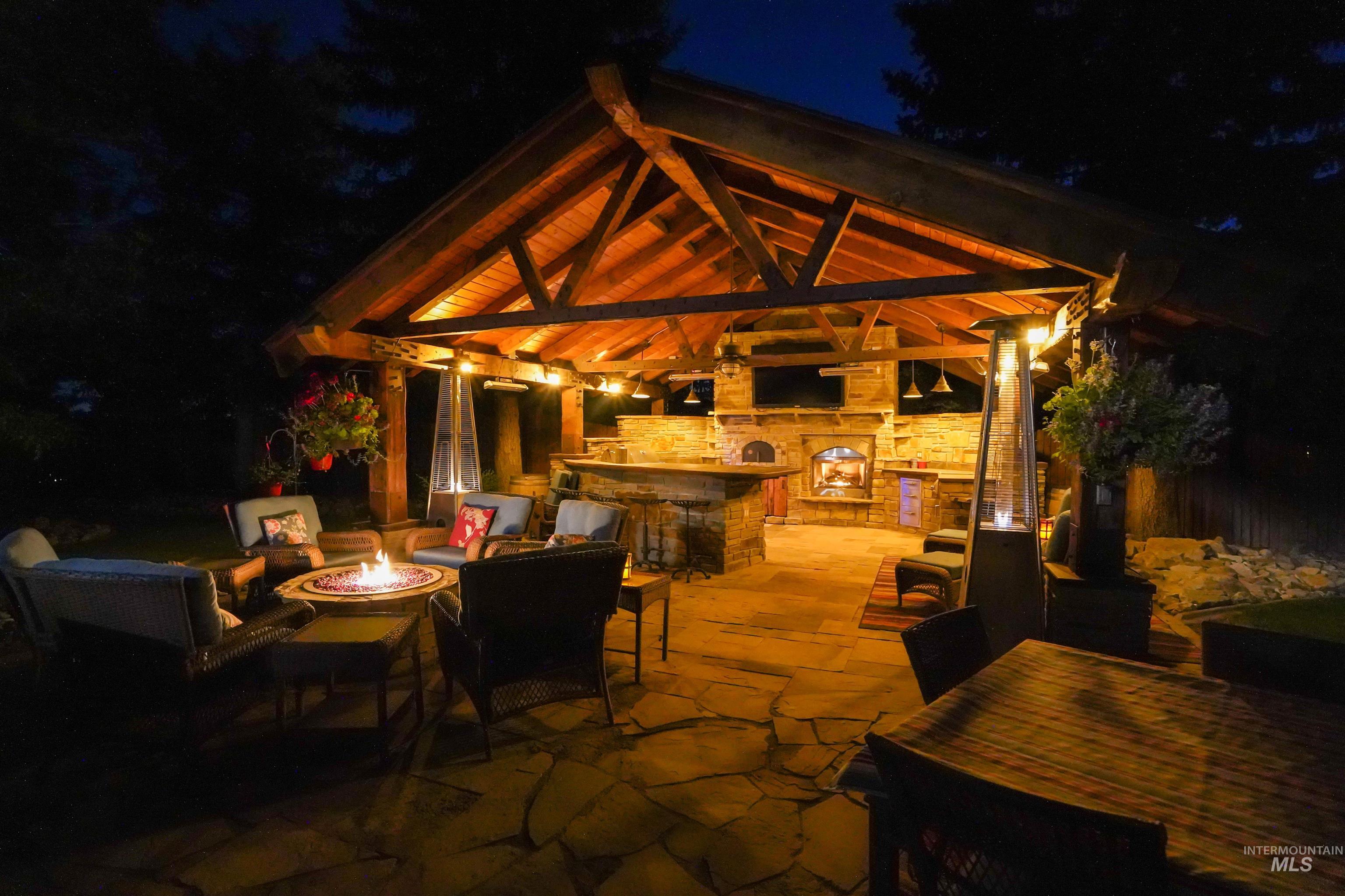 Patio at night with a gazebo, a patio, an outdoor fire pit, and an outdoor stone fireplace