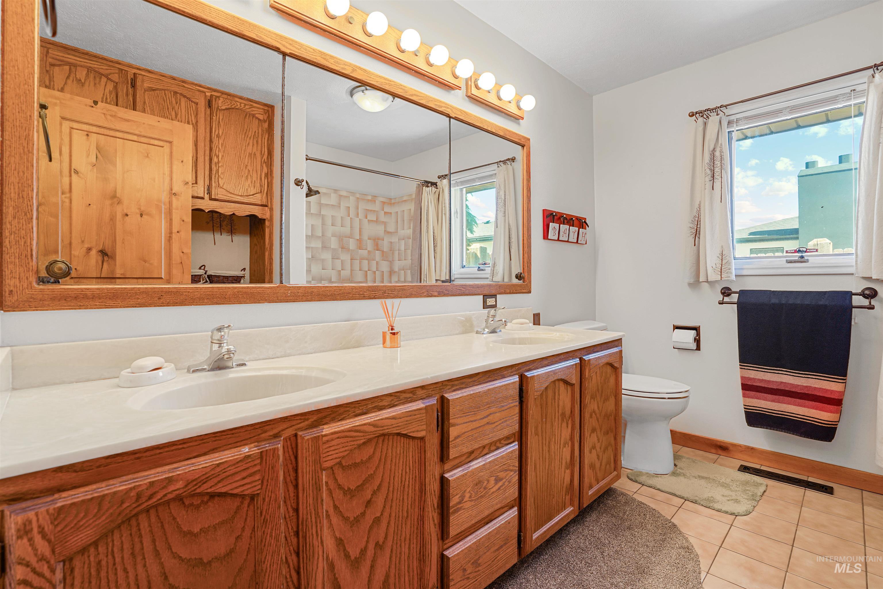 Full bath with double vanity, tile patterned flooring, healthy amount of natural light, and a shower with shower curtain