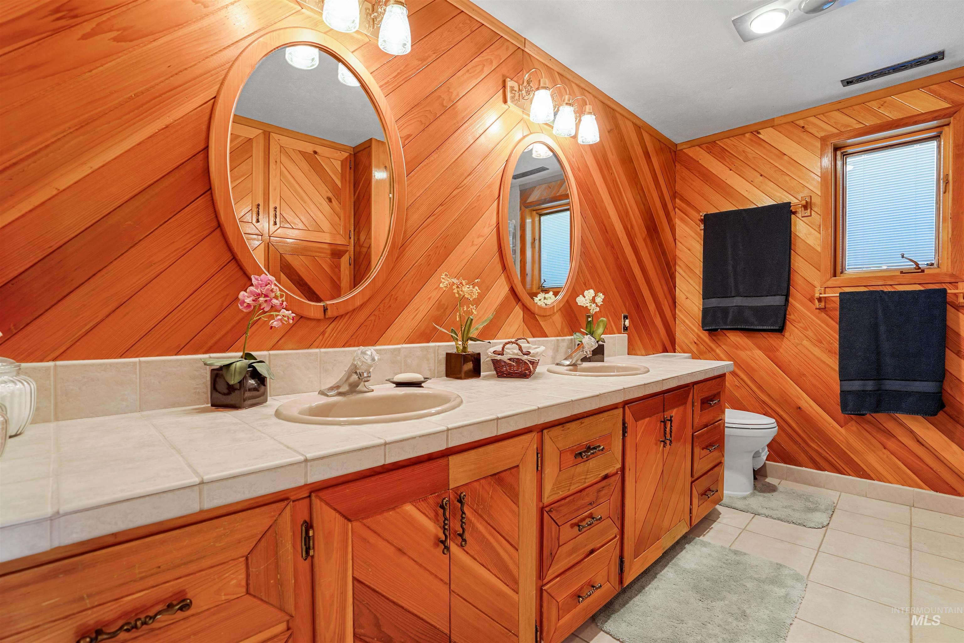 Bathroom featuring double vanity, tile patterned flooring, and wood walls
