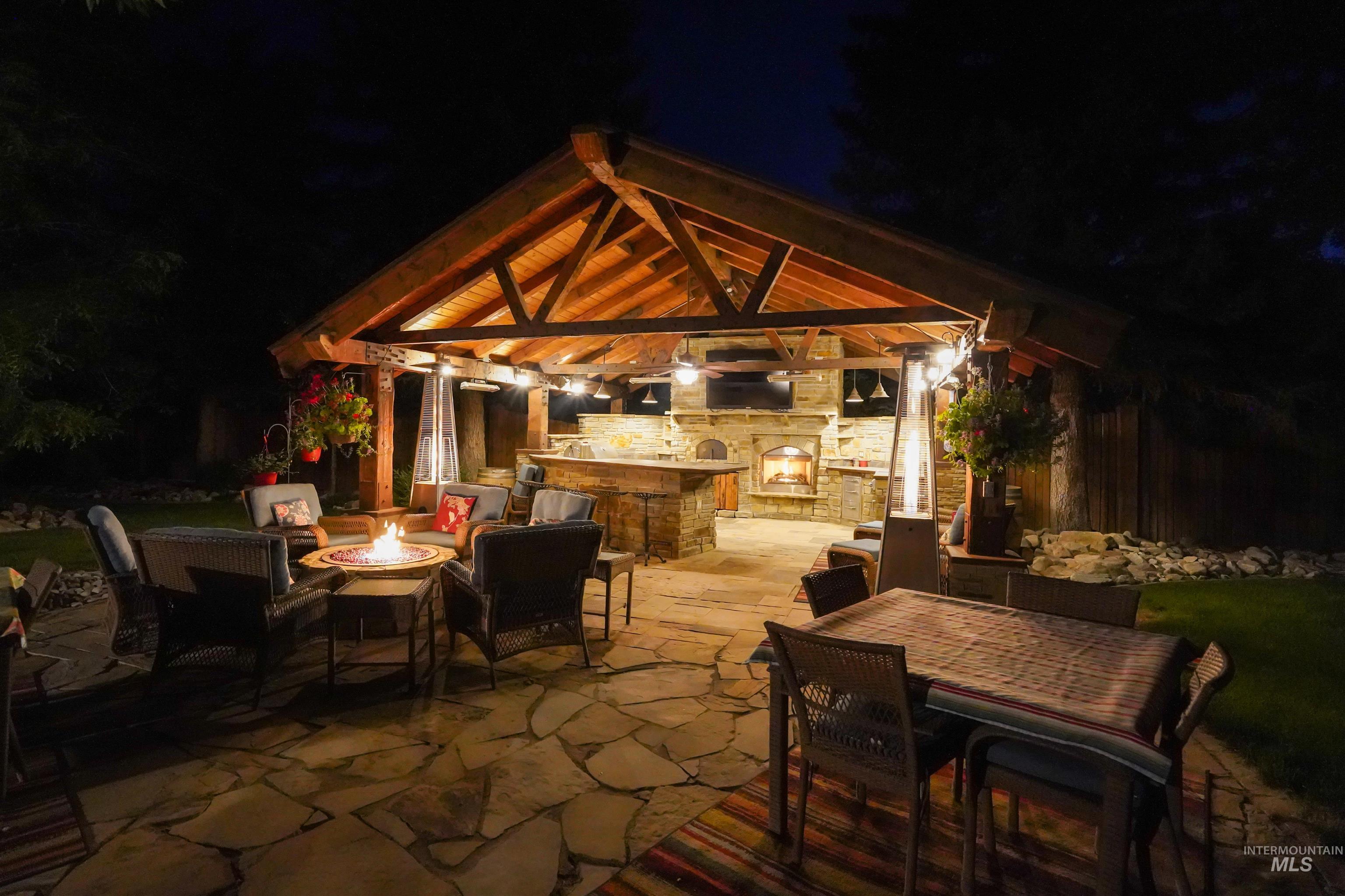 Patio at twilight featuring a gazebo, an outdoor stone fireplace, a patio, an outdoor fire pit, and outdoor dining space