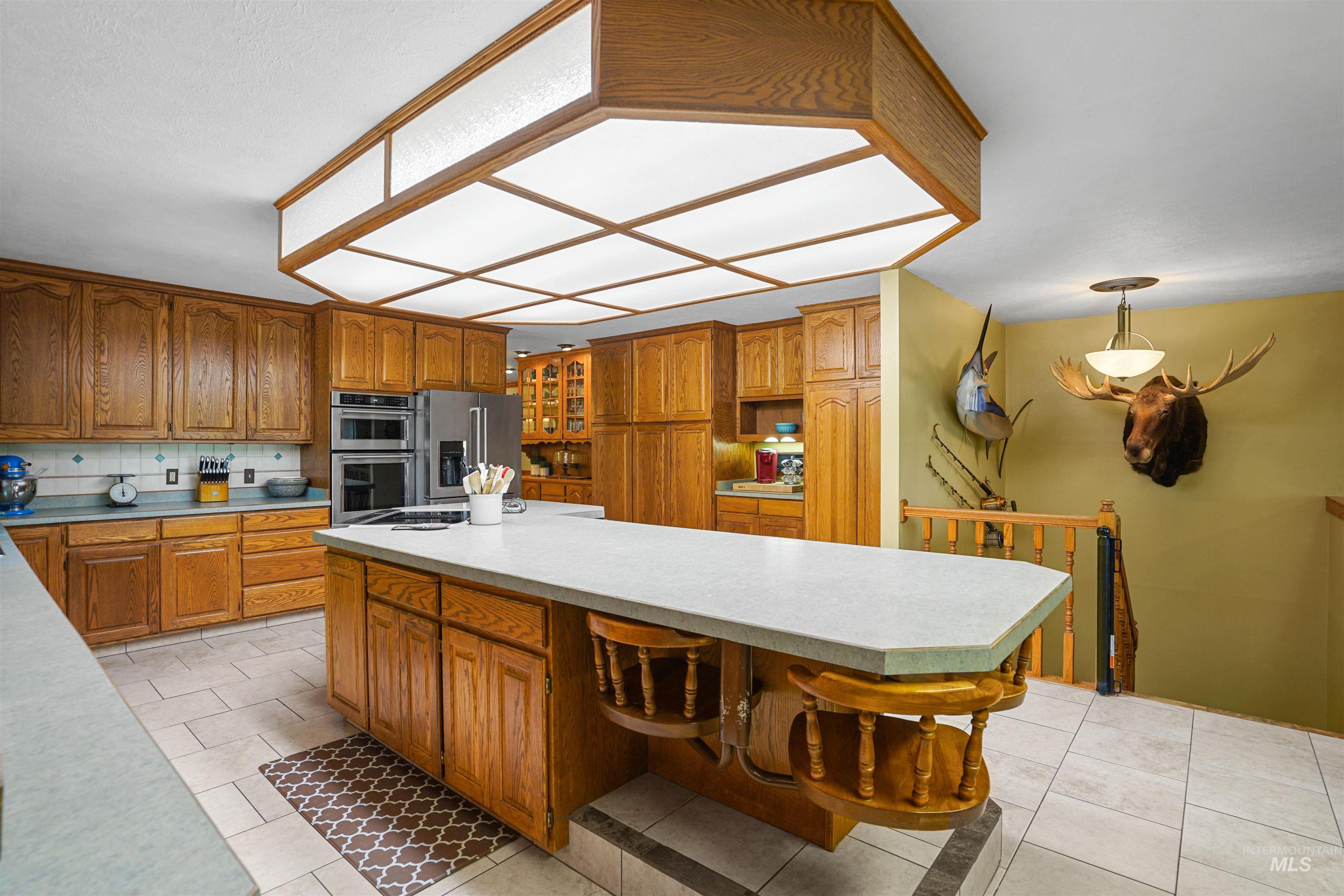 Kitchen with open shelves, brown cabinetry, light countertops, stainless steel appliances, and glass insert cabinets