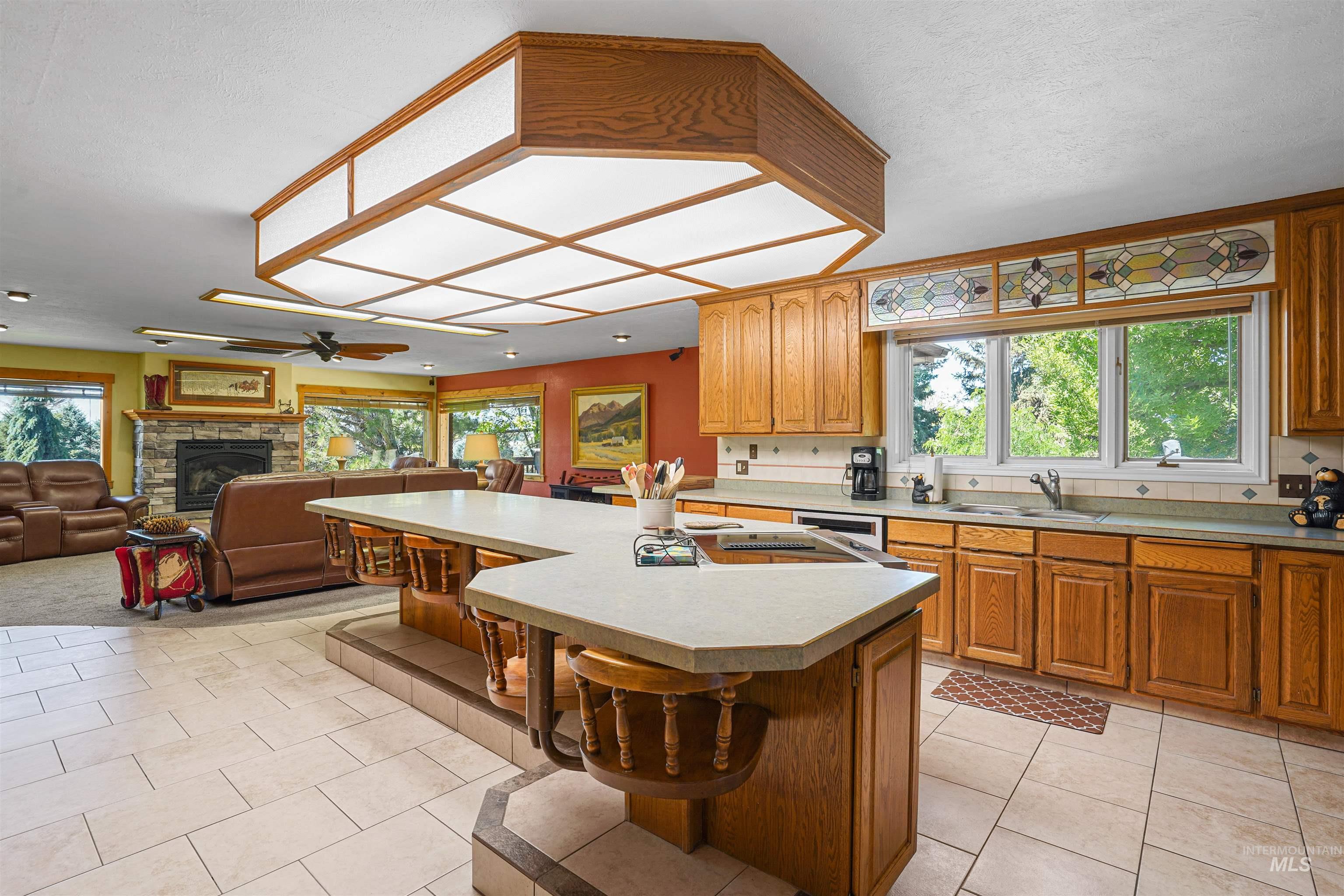 Kitchen with a kitchen bar, a stone fireplace, light countertops, a center island, and a ceiling fan