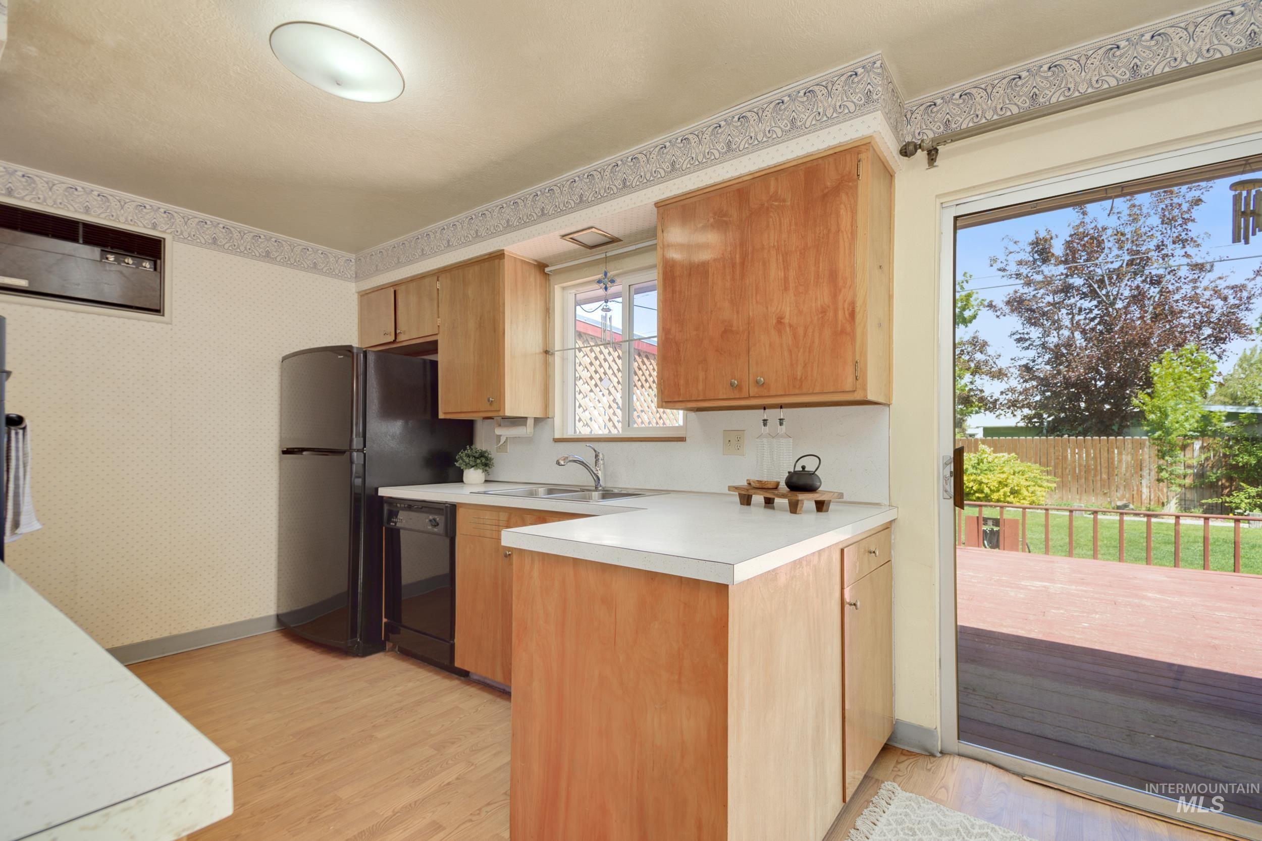 Kitchen featuring light countertops, light wood-style floors, wallpapered walls, a peninsula, and black dishwasher