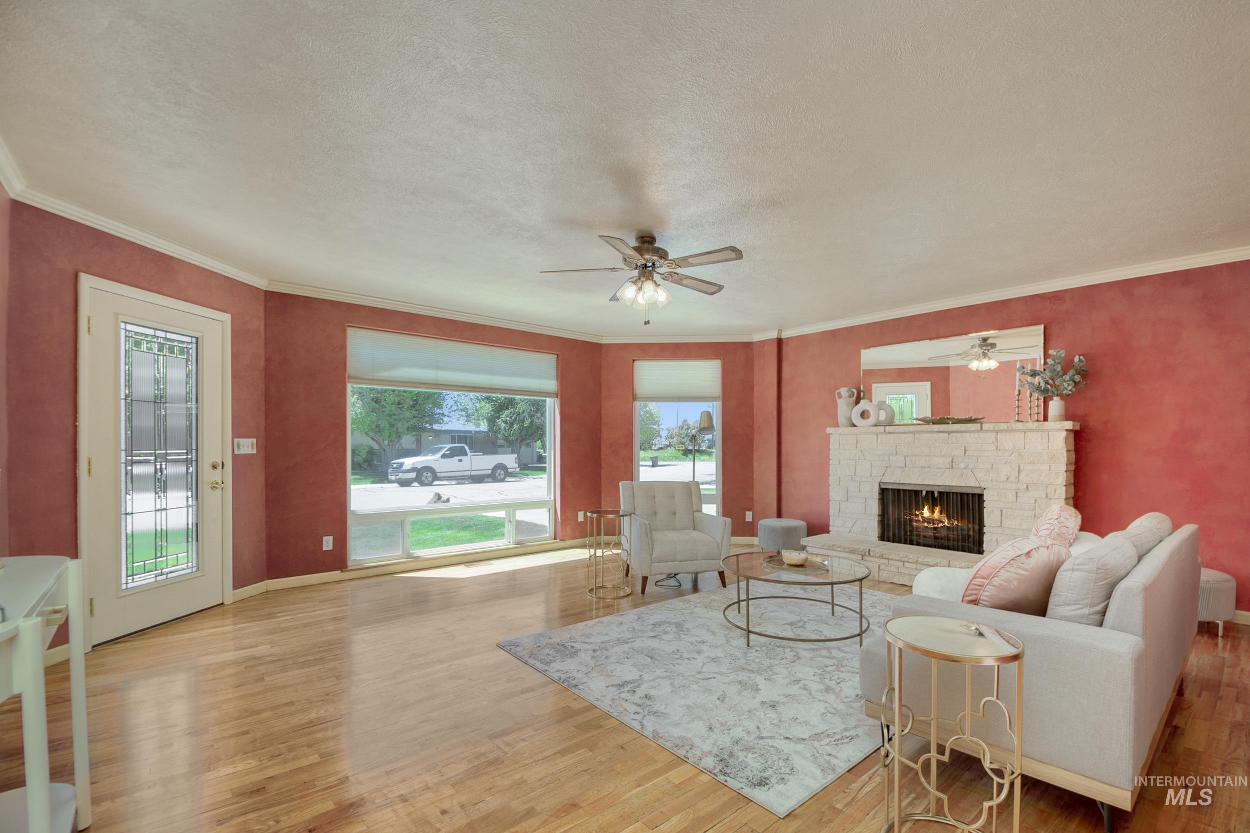 Living area featuring a stone fireplace, crown molding, light wood-type flooring, ceiling fan, and a textured ceiling