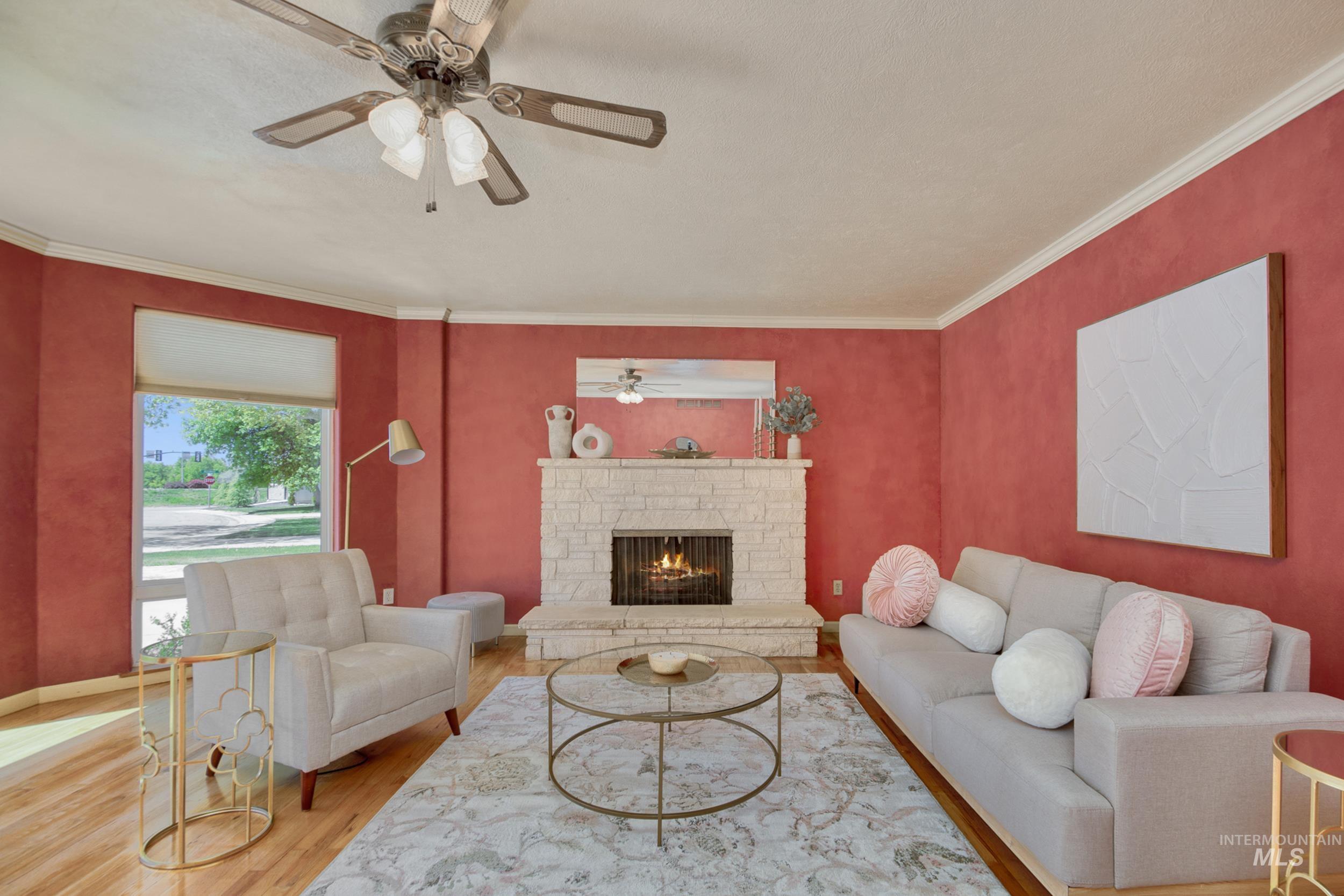 Living area with ornamental molding, wood finished floors, a stone fireplace, and ceiling fan