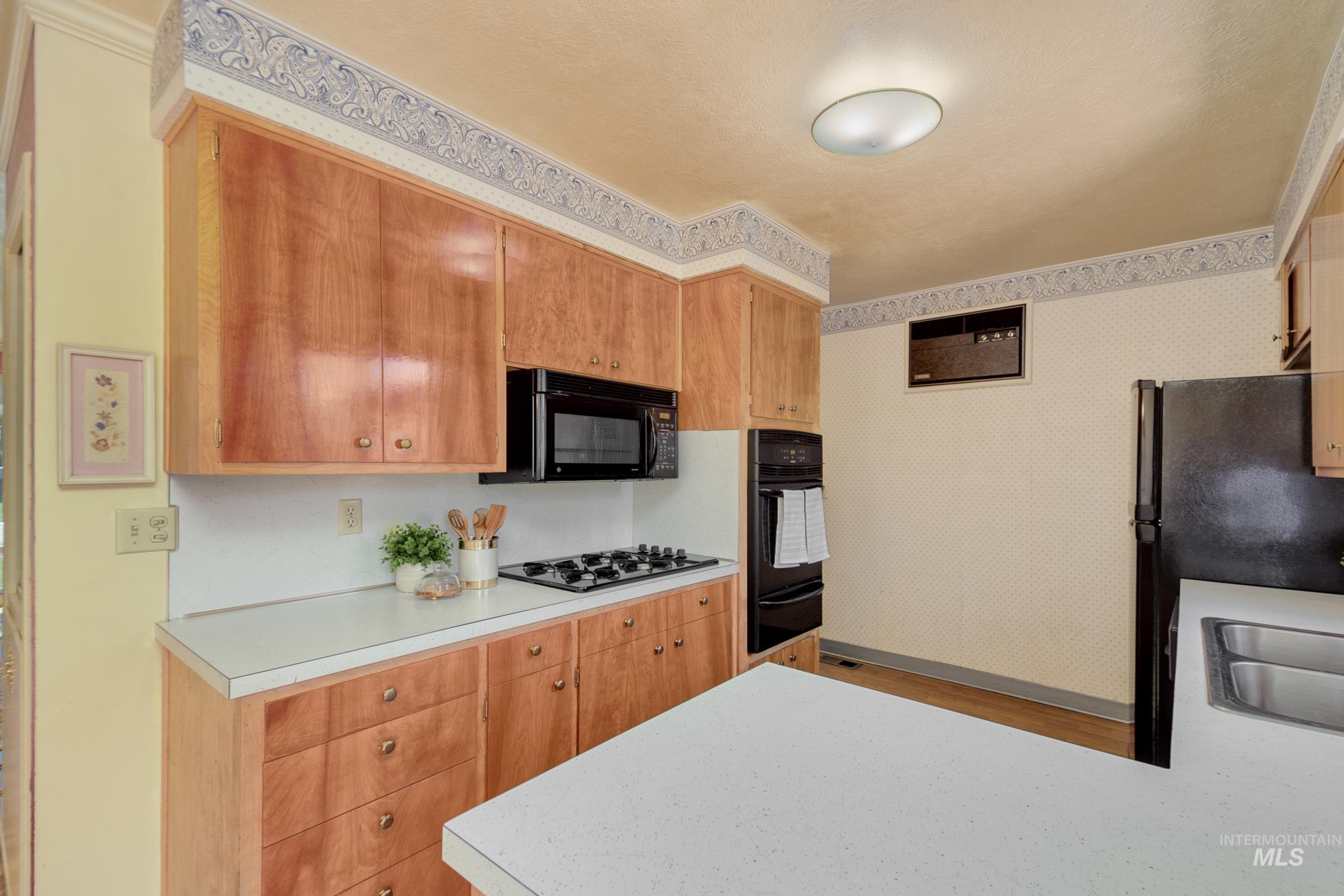 Kitchen with light countertops, black appliances, light wood finished floors, a warming drawer, and a peninsula