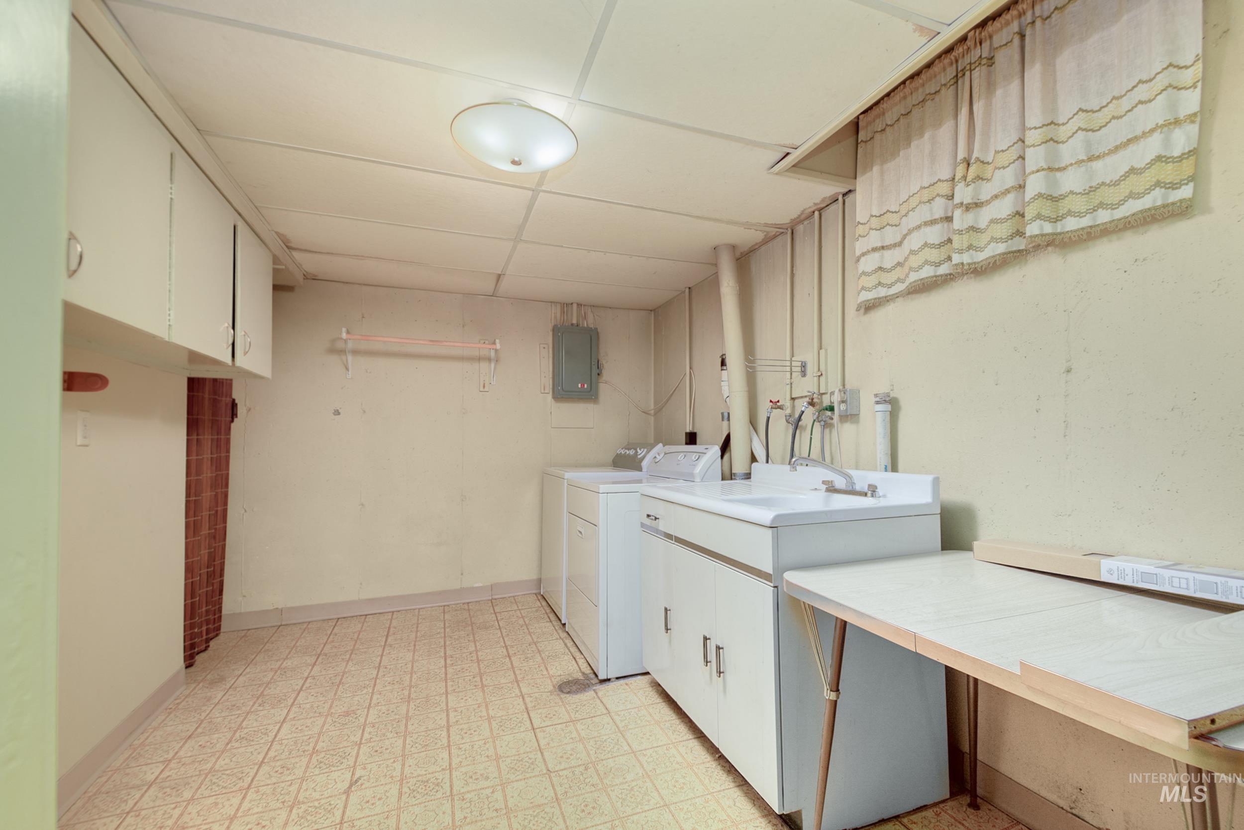 Washroom with light floors, cabinet space, washer and dryer, and electric panel