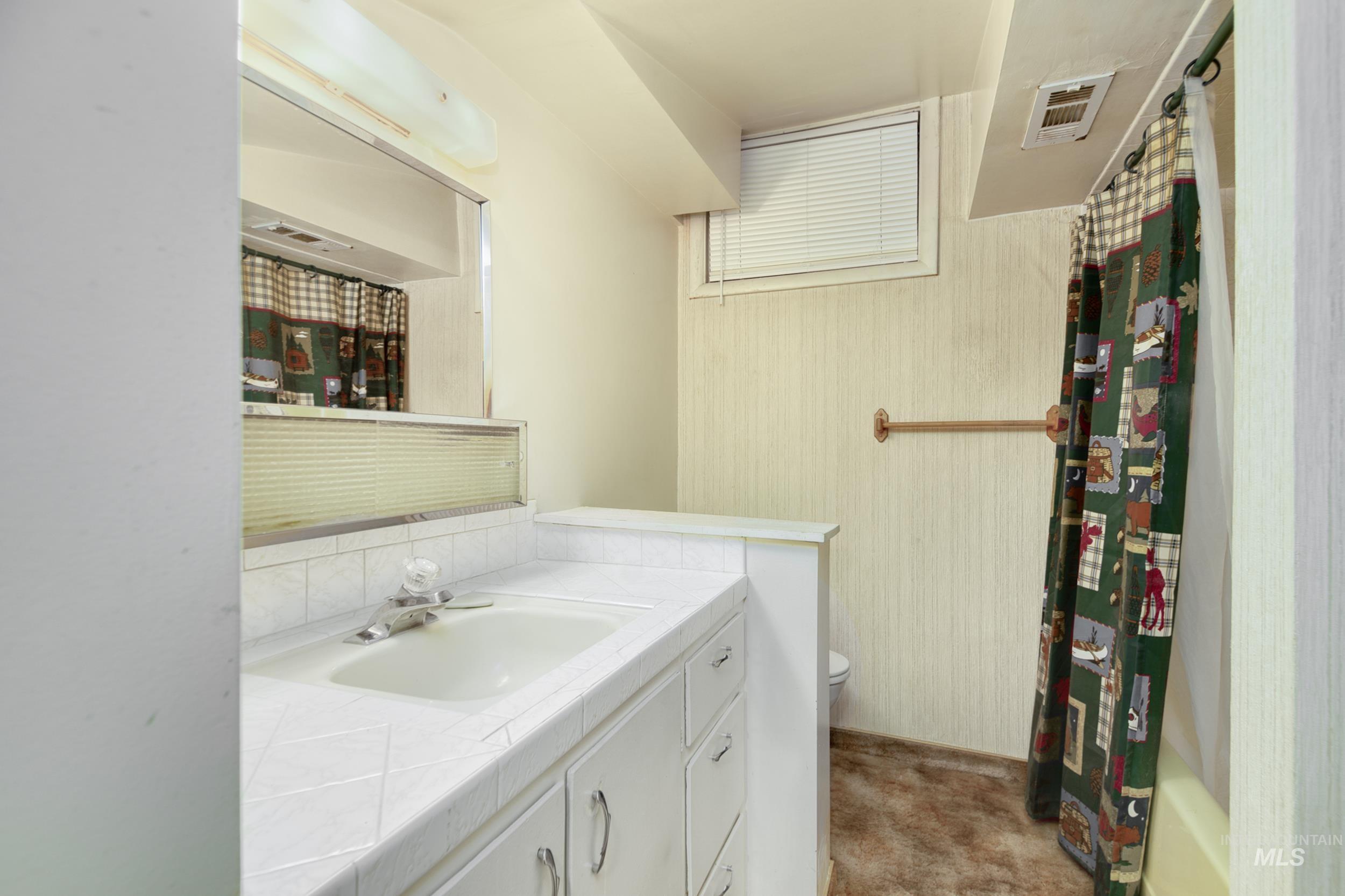 Bathroom with vanity, wallpapered walls, and shower / bath combo