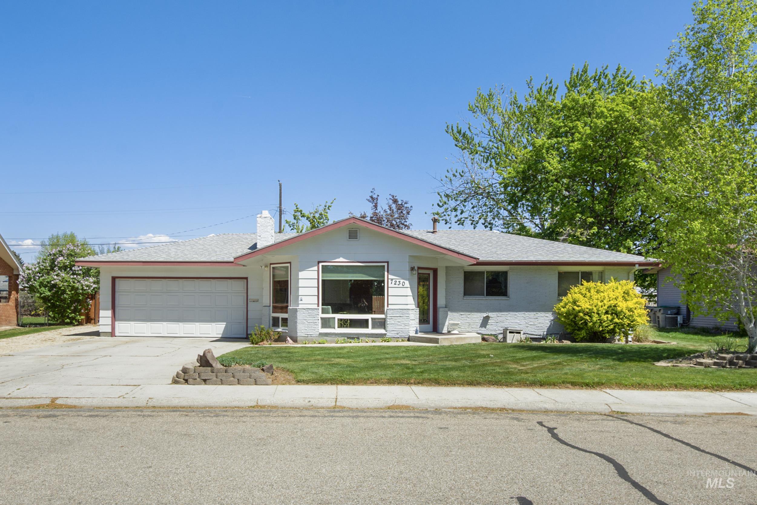 Ranch-style home featuring a front lawn, driveway, a garage, a chimney, and brick siding