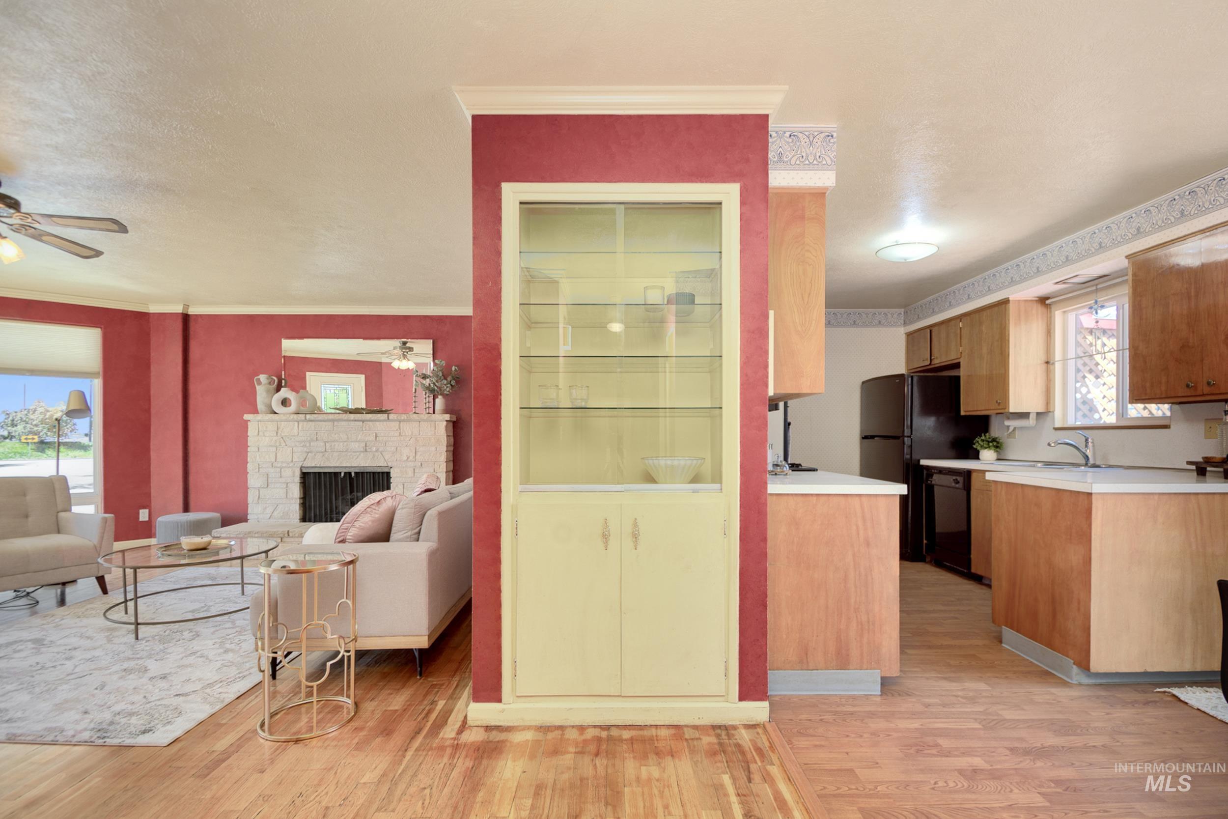 Kitchen featuring light countertops, light wood-type flooring, a stone fireplace, open floor plan, and crown molding