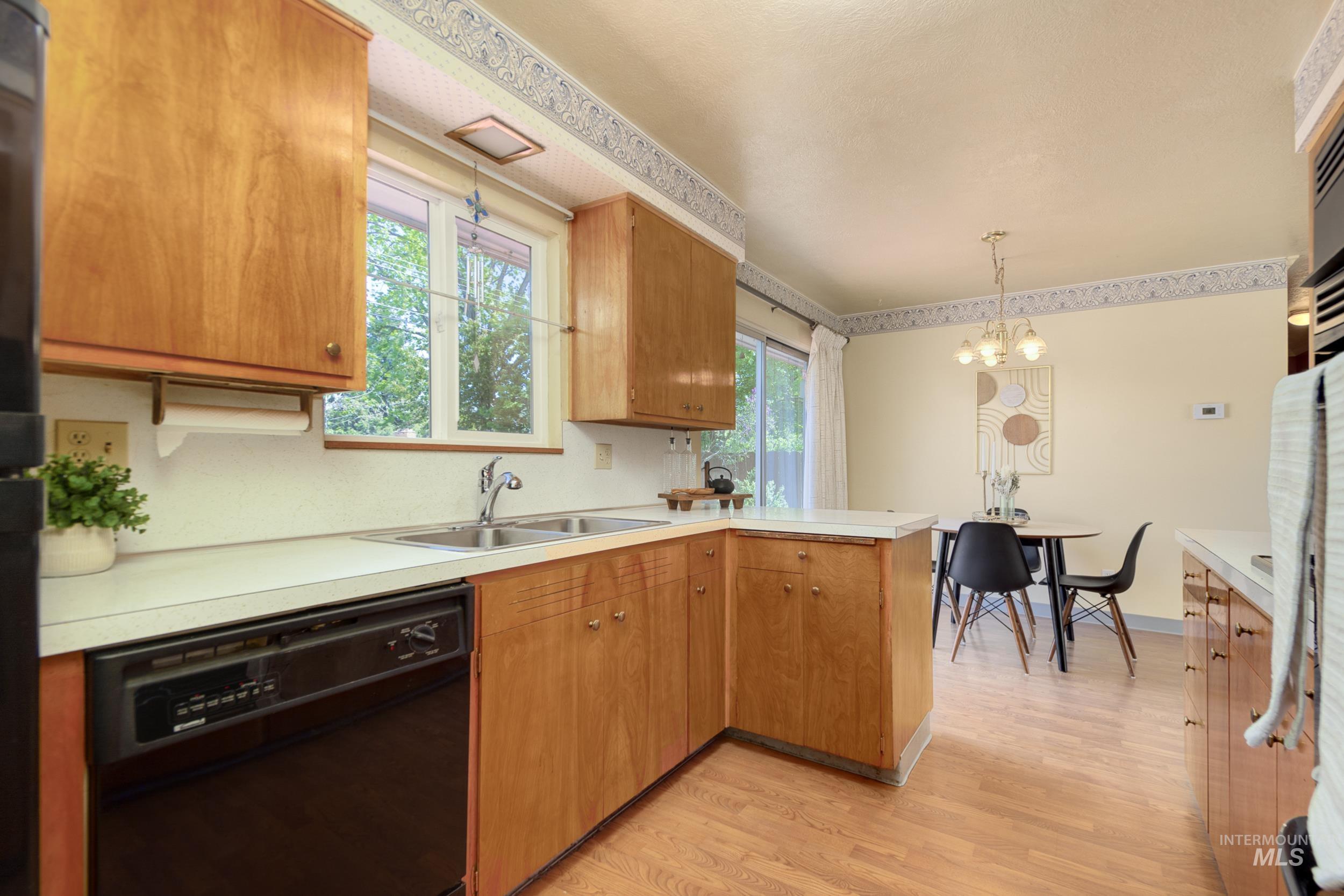 Kitchen with a peninsula, black dishwasher, pendant lighting, light wood-style floors, and light countertops