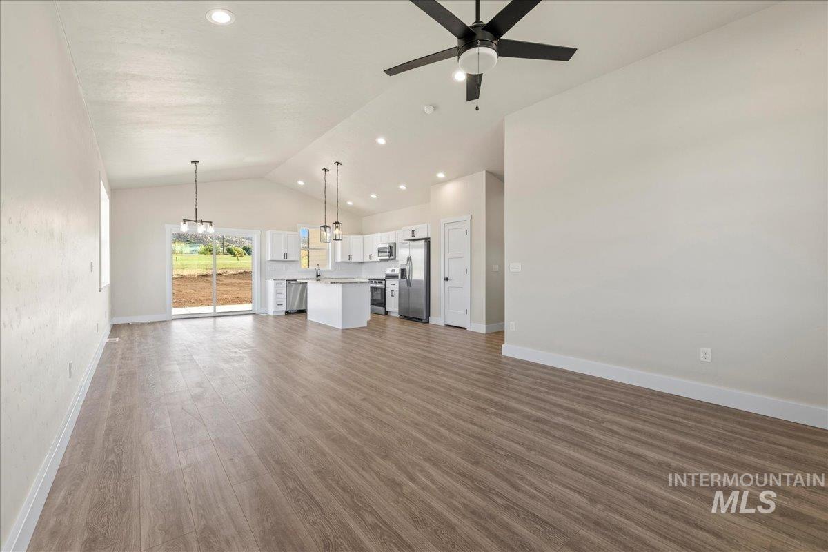 Unfurnished living room featuring dark wood-style floors, recessed lighting, high vaulted ceiling, a chandelier, and ceiling fan