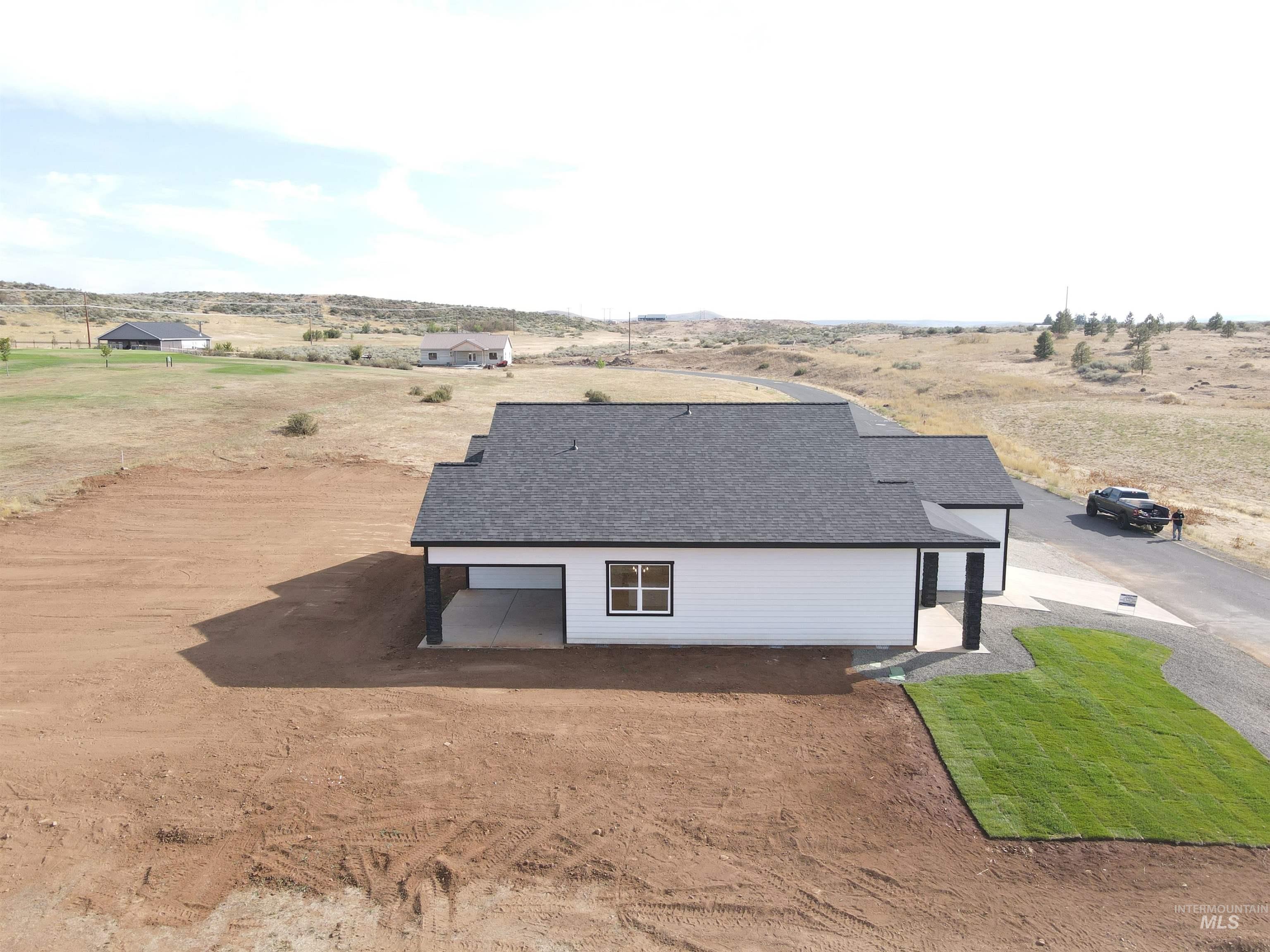 View of side of property with a patio area, a view of countryside, dirt driveway, and a shingled roof