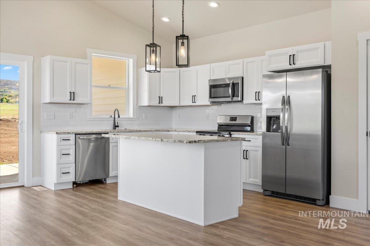 Kitchen with appliances with stainless steel finishes, decorative light fixtures, white cabinetry, light stone countertops, and tasteful backsplash