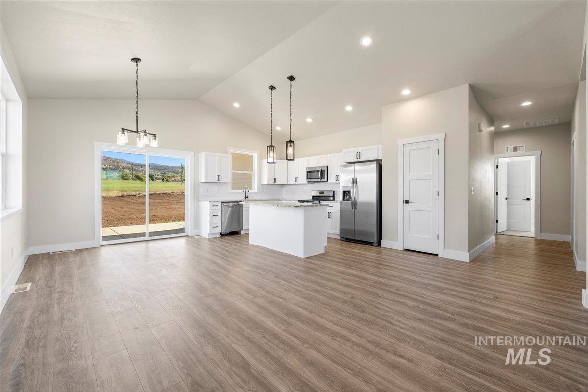 Kitchen featuring hanging light fixtures, open floor plan, stainless steel appliances, white cabinetry, and a center island