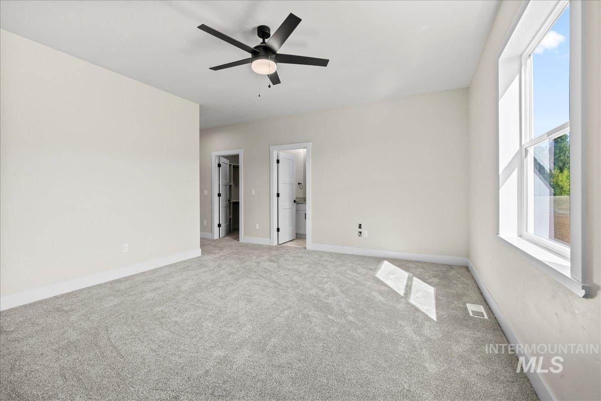 Unfurnished bedroom featuring carpet floors, a walk in closet, a ceiling fan, and ensuite bathroom
