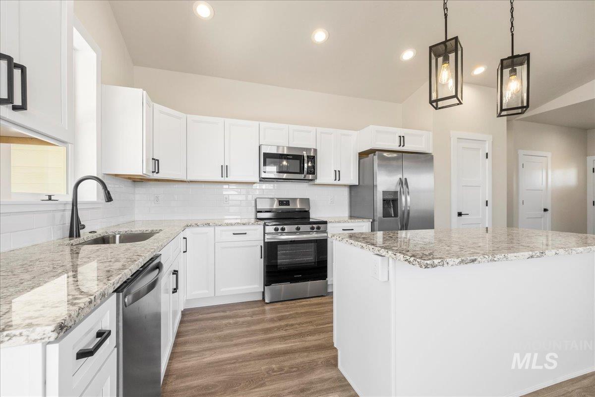 Kitchen with pendant lighting, appliances with stainless steel finishes, a kitchen island, decorative backsplash, and white cabinets