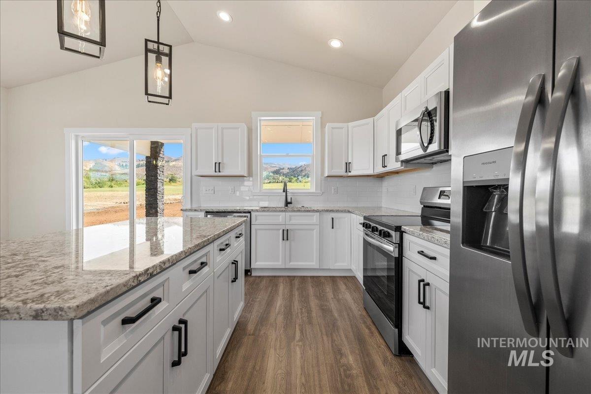 Kitchen with appliances with stainless steel finishes, white cabinets, pendant lighting, decorative backsplash, and dark wood finished floors