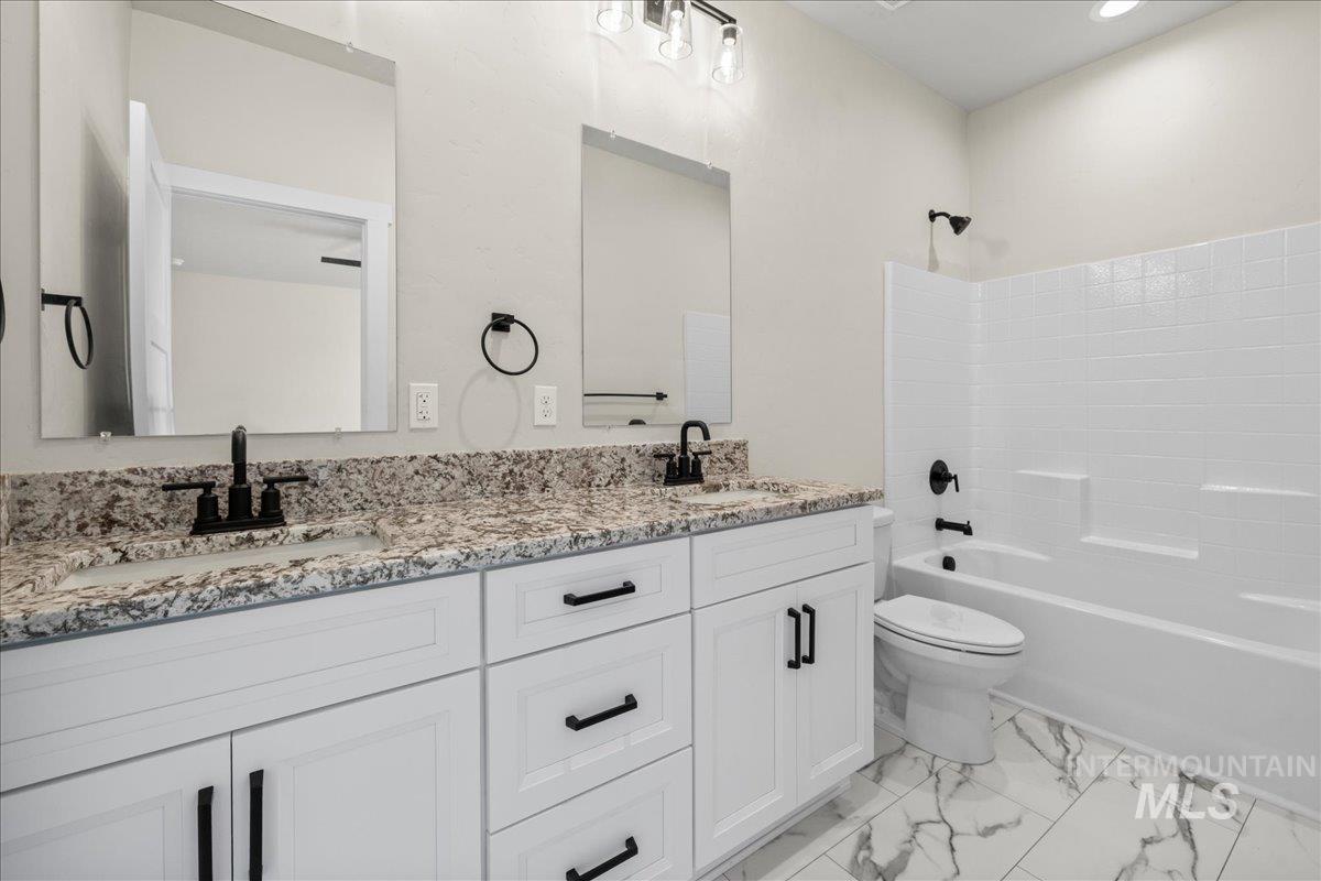 Bathroom with shower / bath combination, double vanity, and light marble finish flooring