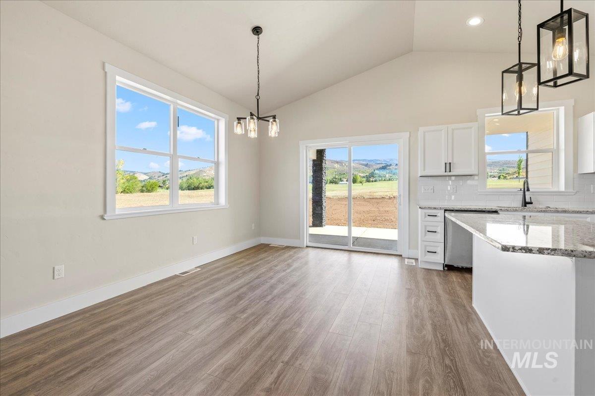 Unfurnished dining area featuring a chandelier, healthy amount of natural light, dark wood-style floors, high vaulted ceiling, and recessed lighting