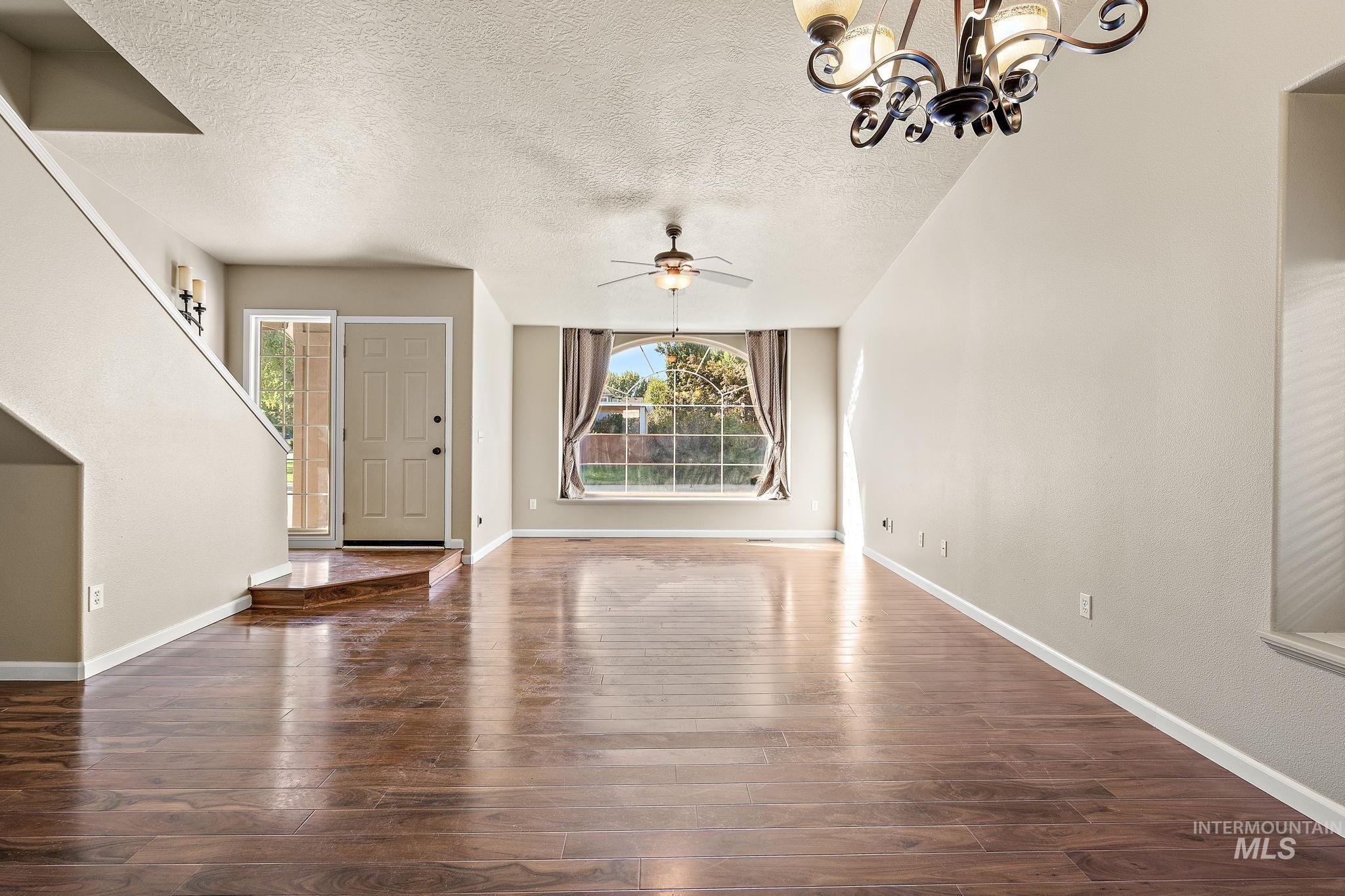 Unfurnished living room featuring healthy amount of natural light, a textured ceiling, a chandelier, a ceiling fan, and dark wood finished floors