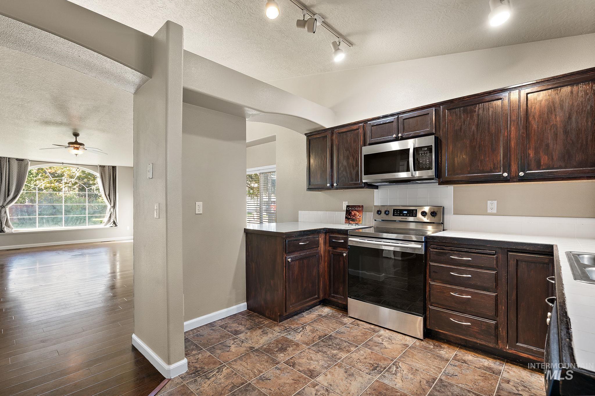 Kitchen featuring dark brown cabinetry, a textured ceiling, appliances with stainless steel finishes, plenty of natural light, and light countertops