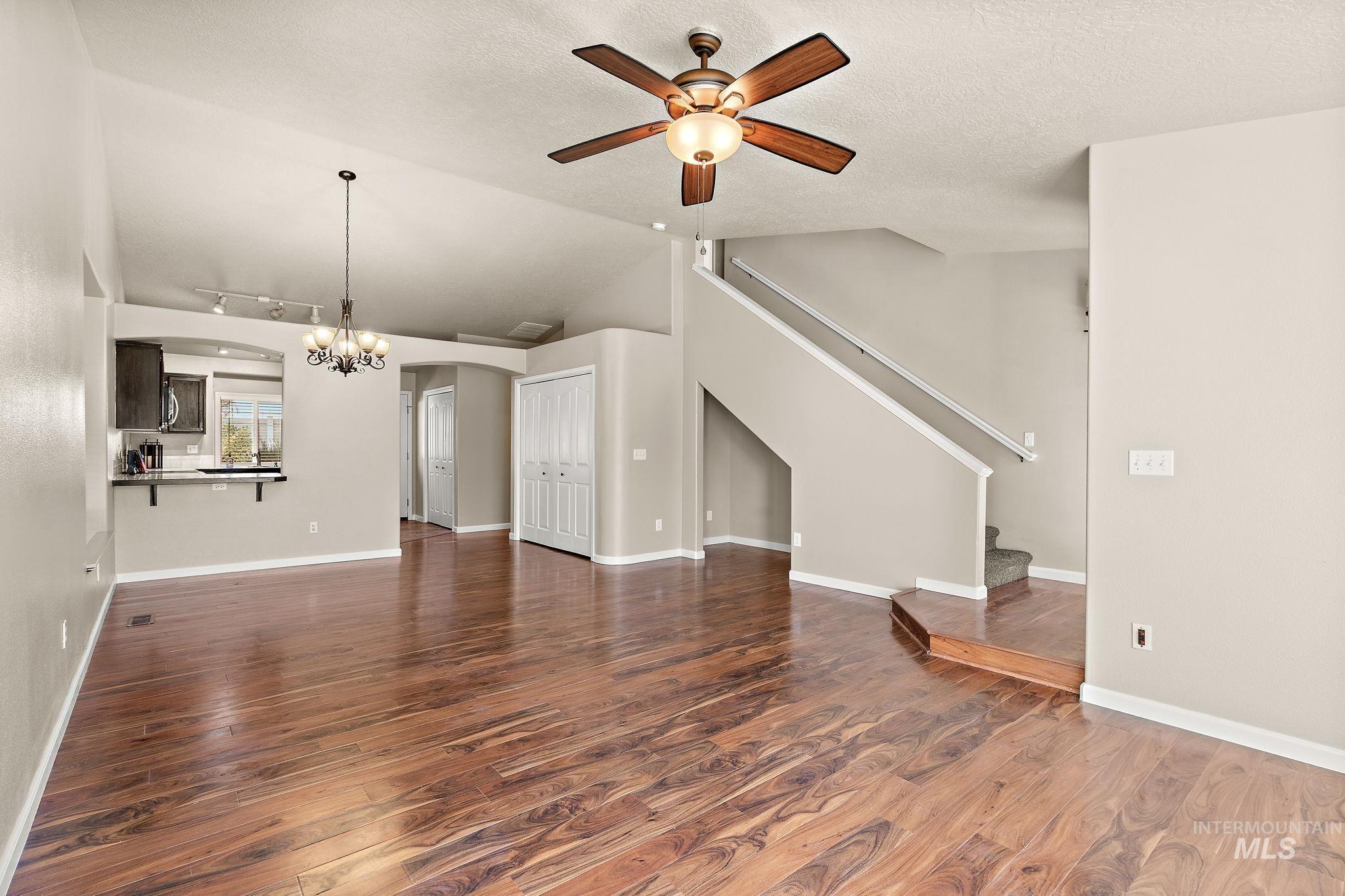 Unfurnished living room featuring dark wood-style floors, a textured ceiling, a ceiling fan, a chandelier, and vaulted ceiling