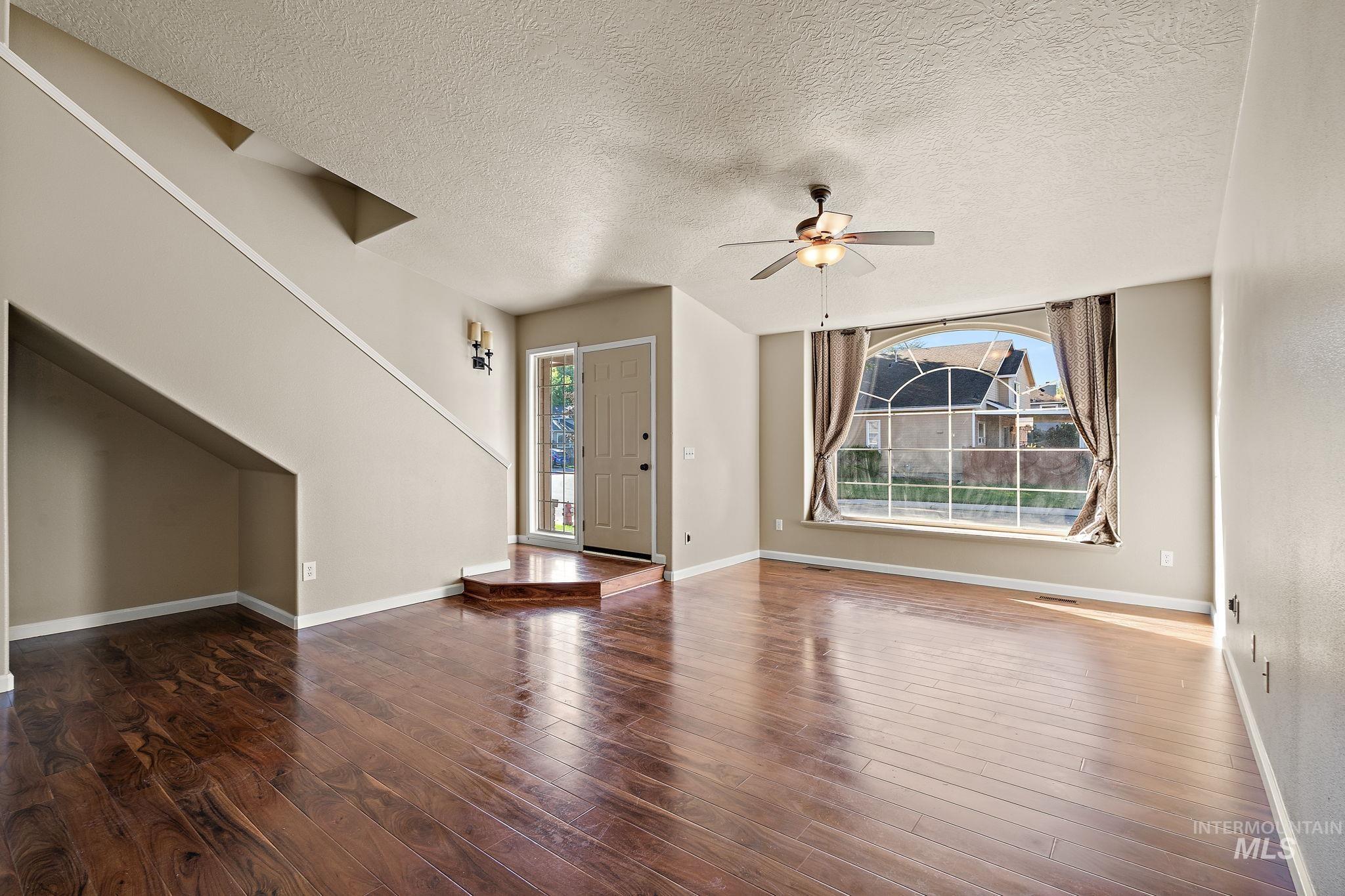 Unfurnished living room with a textured ceiling, healthy amount of natural light, a ceiling fan, and dark wood-type flooring