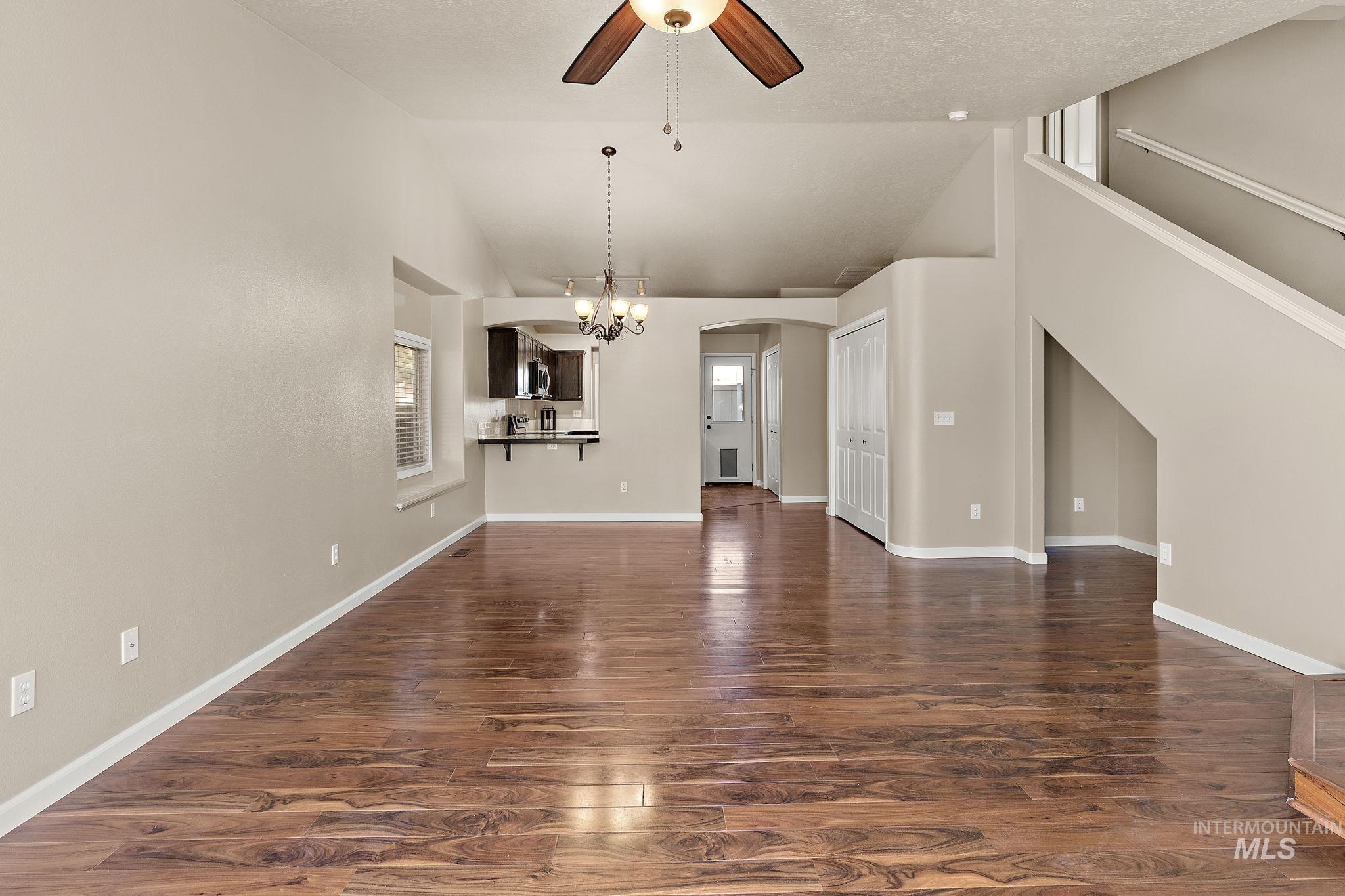 Unfurnished living room with dark wood-type flooring, vaulted ceiling, a ceiling fan, a chandelier, and arched walkways