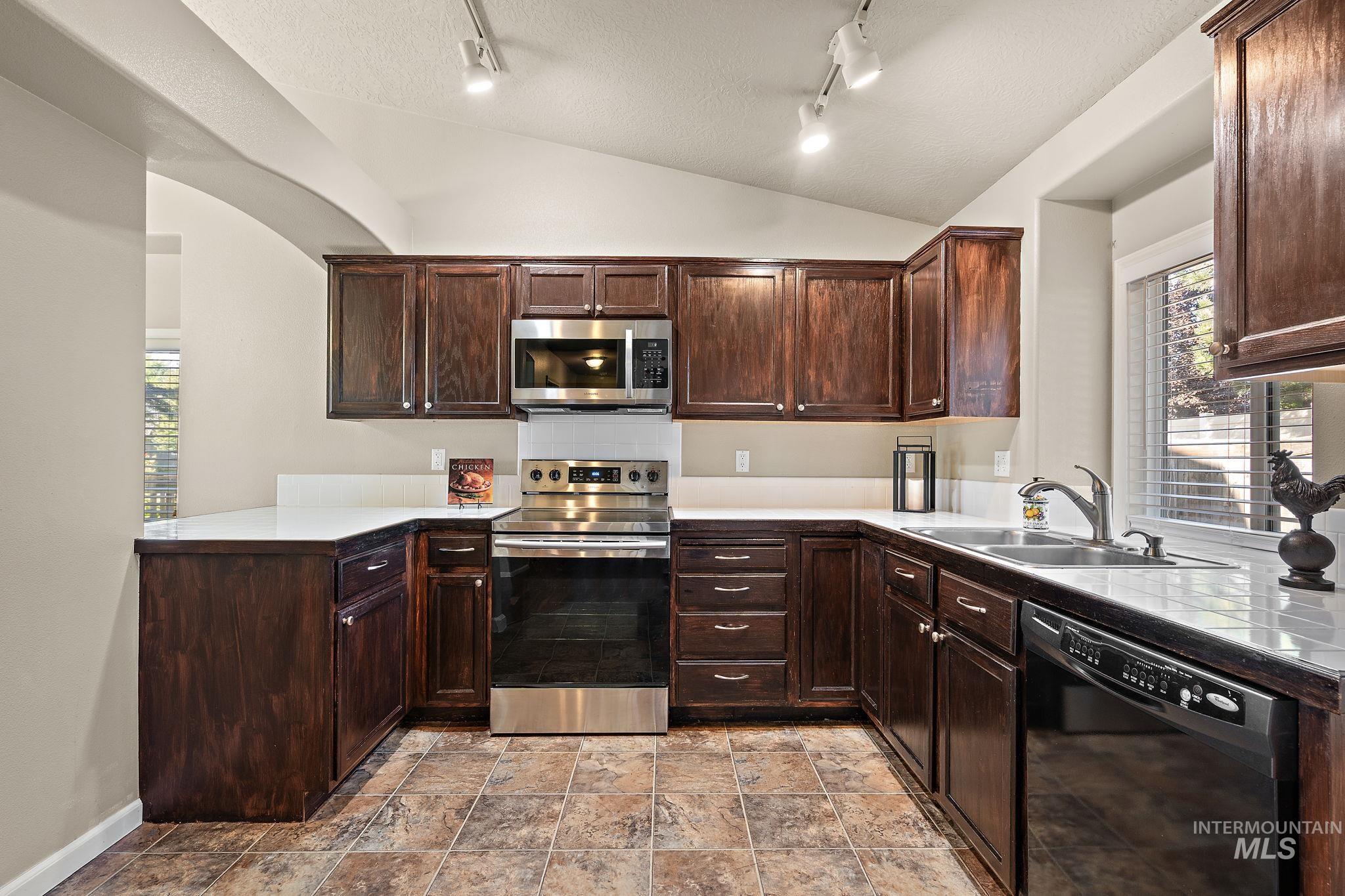 Kitchen with appliances with stainless steel finishes, dark brown cabinetry, lofted ceiling, track lighting, and a textured ceiling