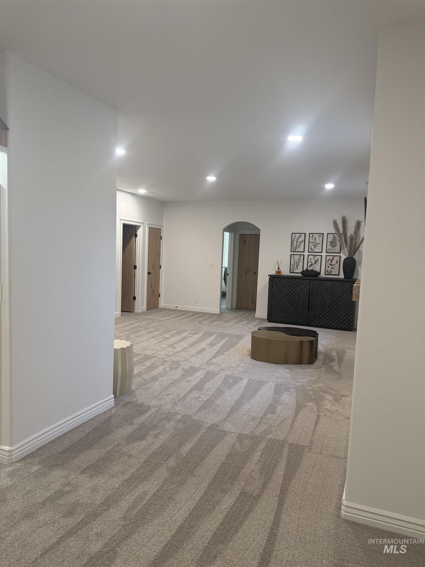Unfurnished living room featuring arched walkways, recessed lighting, and light colored carpet