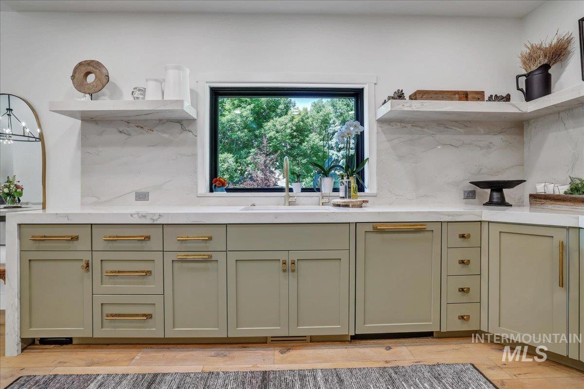 Kitchen featuring green cabinetry, decorative backsplash, open shelves, light countertops, and light wood-style flooring