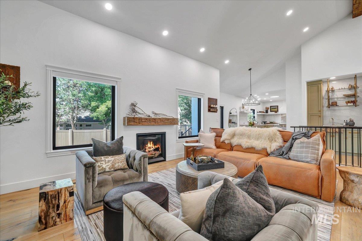 Living room with light wood finished floors, recessed lighting, a glass covered fireplace, and high vaulted ceiling