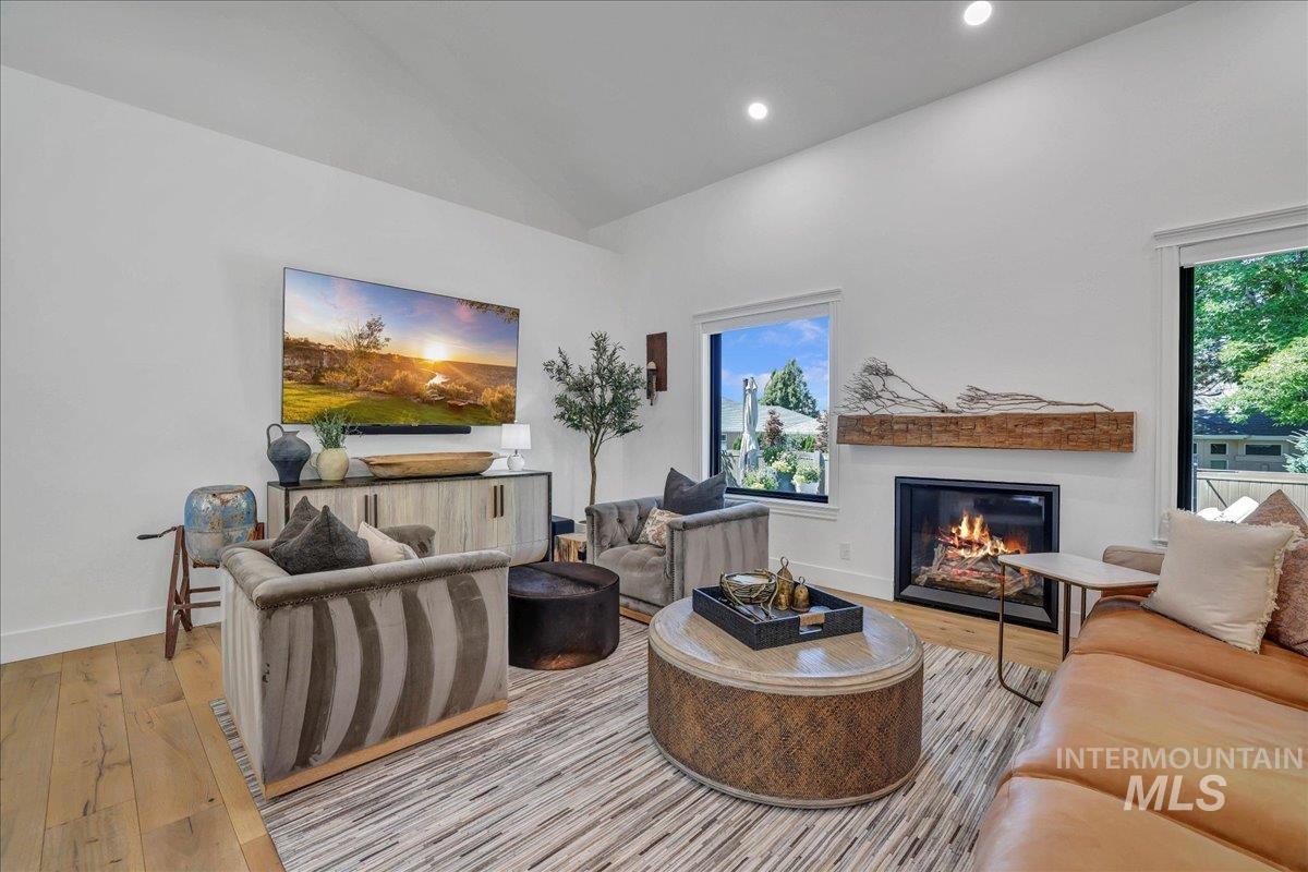 Living room featuring vaulted ceiling, a glass covered fireplace, wood finished floors, and recessed lighting