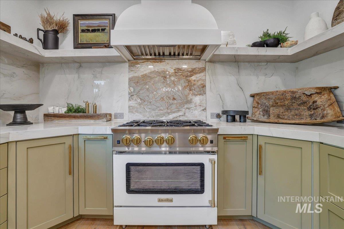 Kitchen featuring high end stainless steel range oven, light countertops, custom range hood, open shelves, and green cabinetry