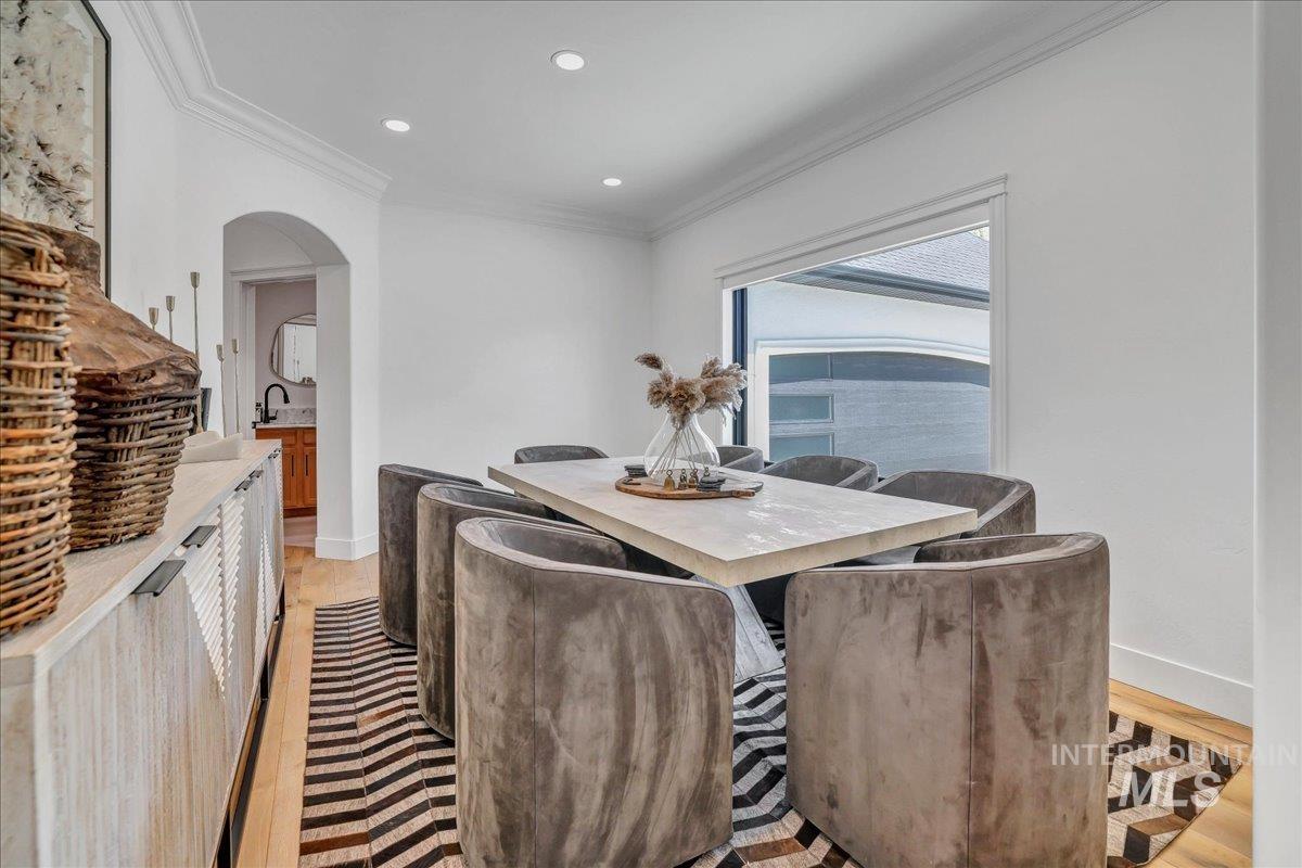 Dining room with crown molding, arched walkways, light wood finished floors, and recessed lighting