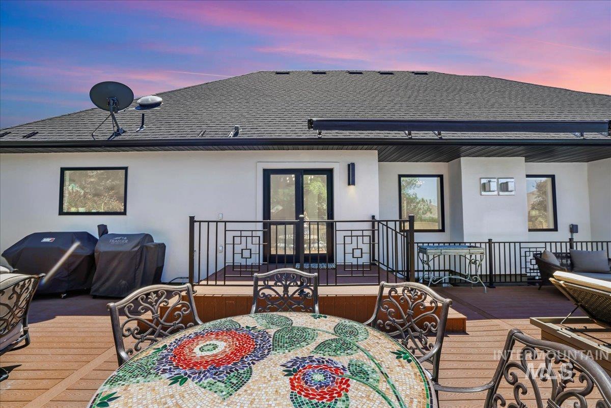 Back of house at dusk with outdoor dining space, stucco siding, roof with shingles, a wooden deck, and french doors