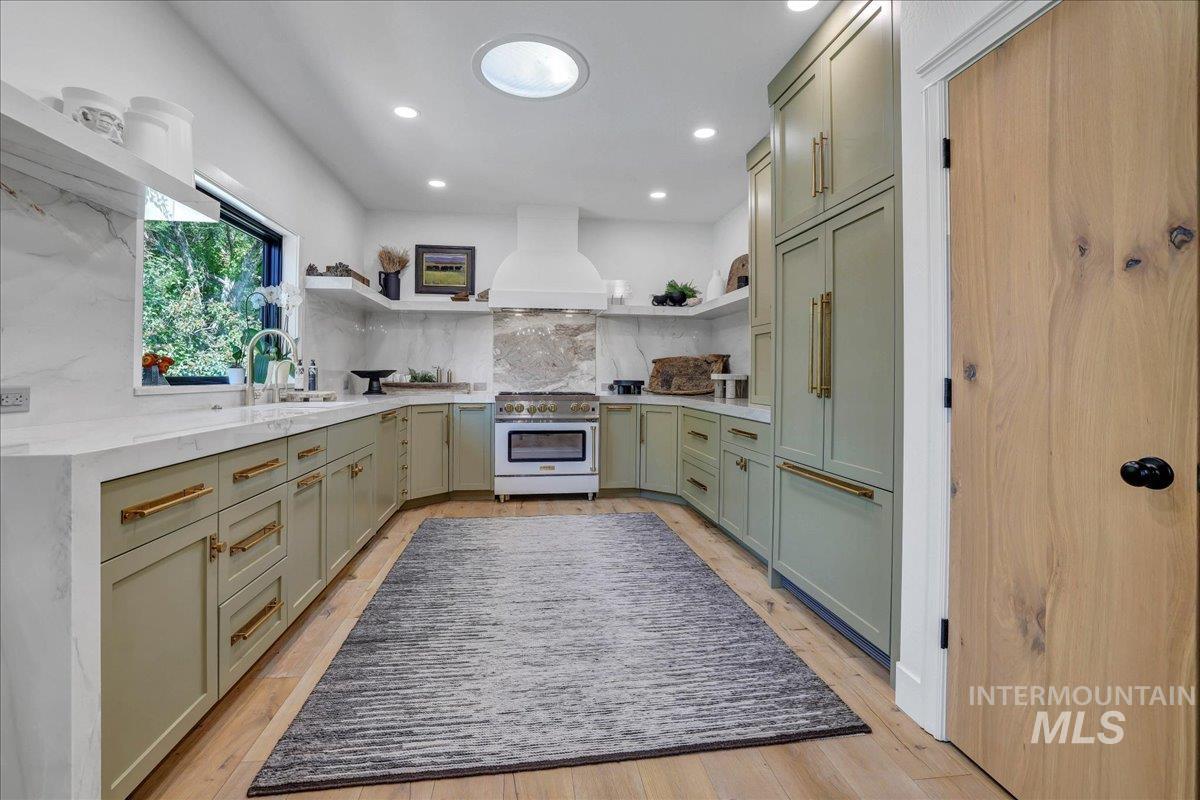 Kitchen with open shelves, green cabinetry, high end stainless steel range oven, tasteful backsplash, and custom range hood