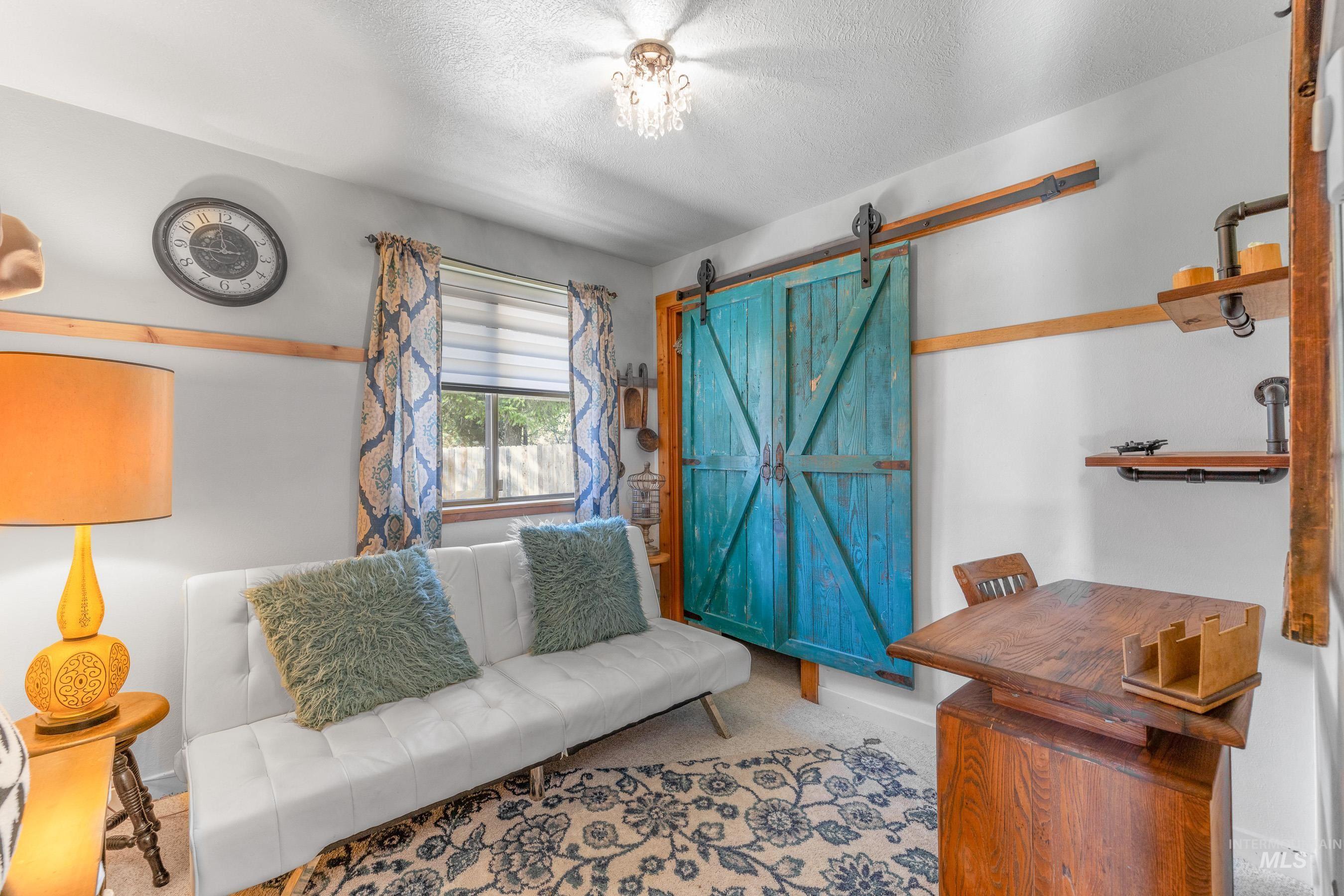 Interior space featuring a teal-painted barn door, industrial-style shelving, a window with blinds and patterned curtains, a white upholstered sofa, and a wood-finish desk
