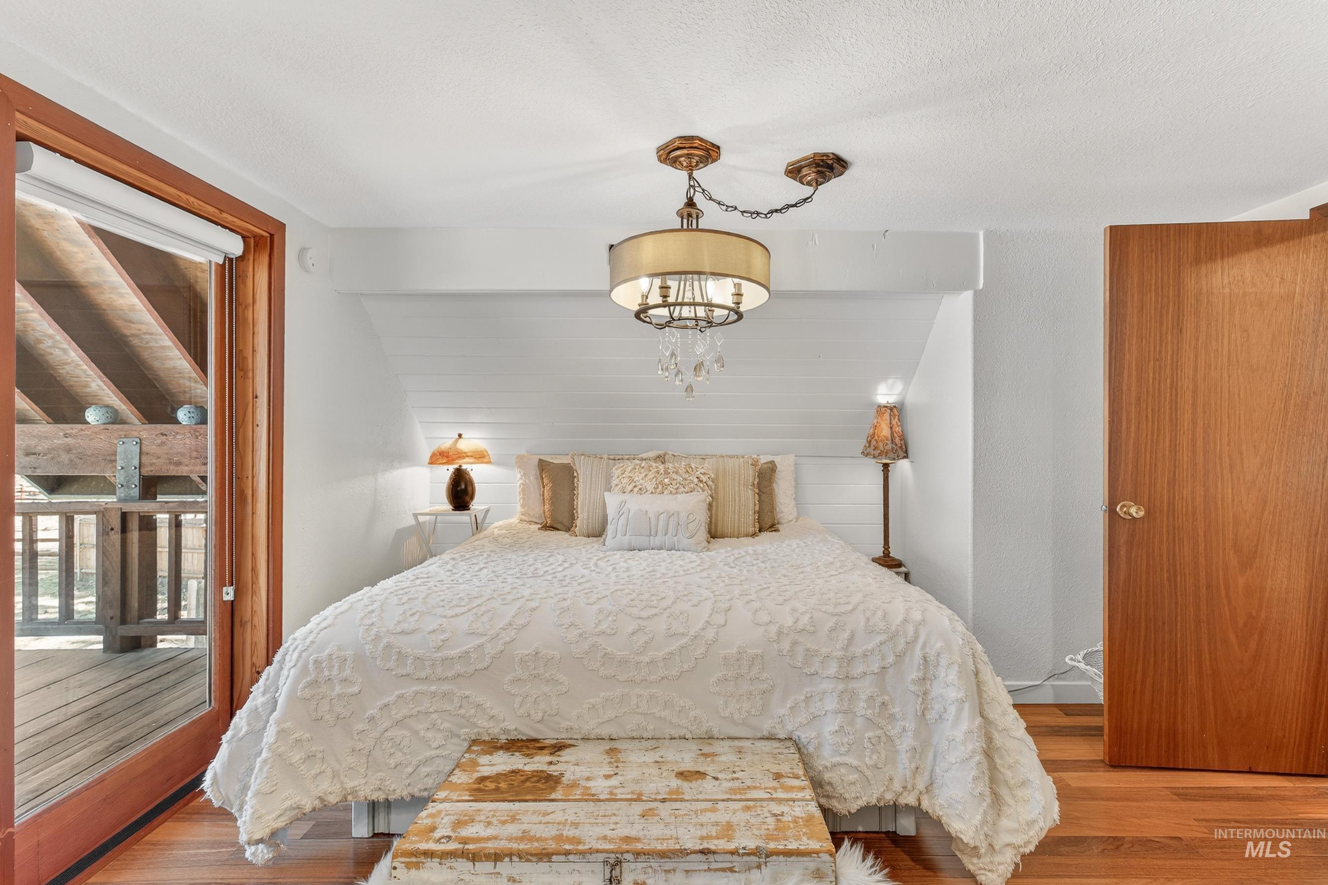 Hardwood flooring throughout this room, featuring a built-in shiplap headboard wall, and a decorative ceiling light fixture with crystal accents