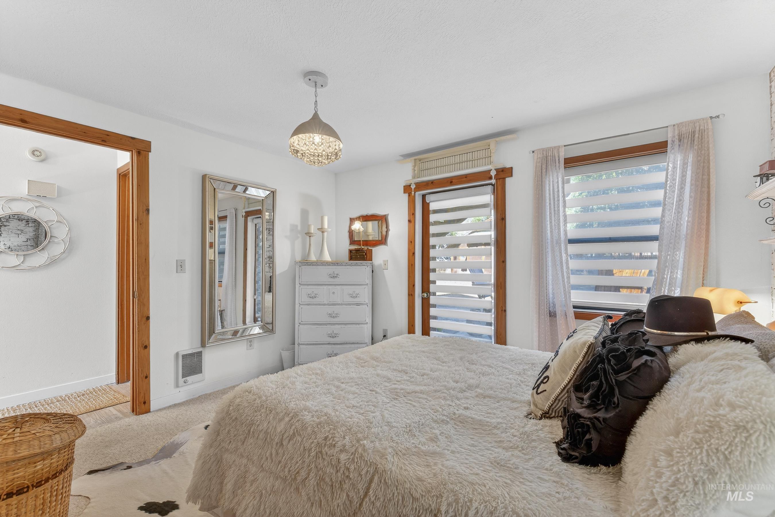 Bedroom with light wood-trimmed windows and door frame, wall-to-wall carpeting, and a crystal chandelier