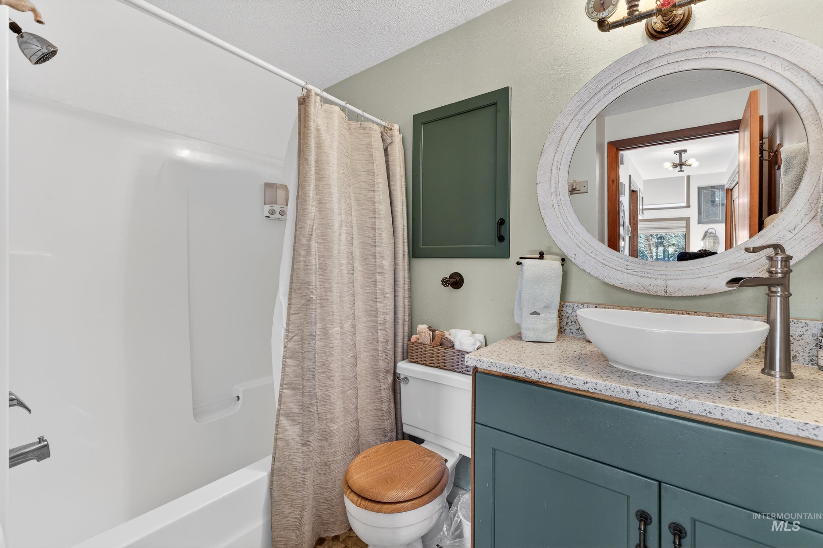 Bathroom featuring a white tub-shower combination, a vanity with a white vessel sink, a speckled countertop, and a distressed white circular mirror