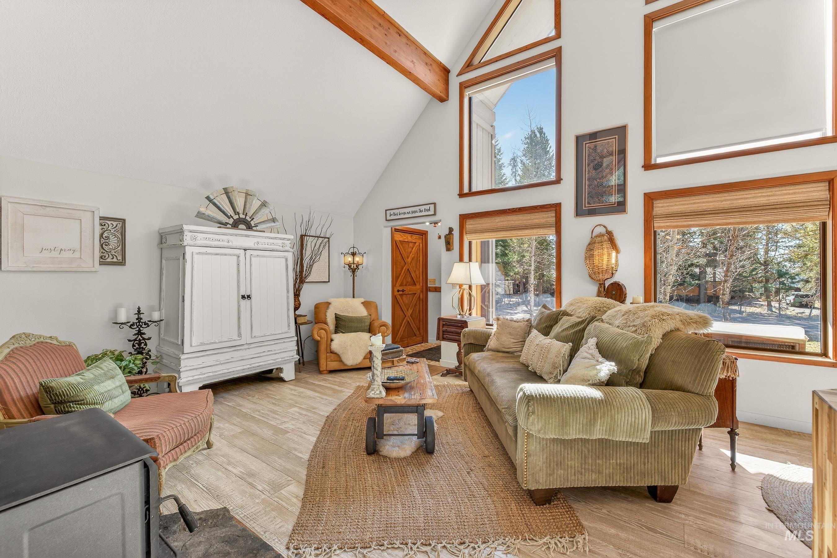 Vaulted ceilings with exposed wood beams, wood-finish flooring, multiple windows with natural wood trim, and a built-in wood-burning stove