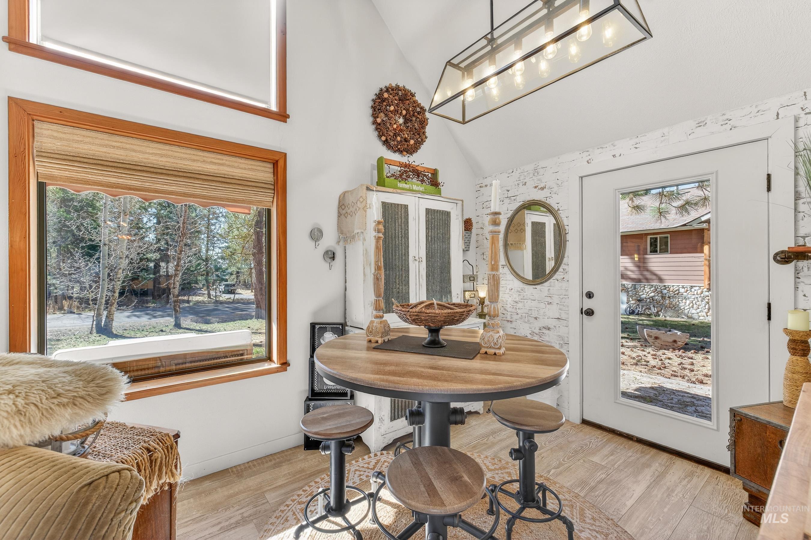 Vaulted ceilings with a rectangular pendant light fixture, wood-finish flooring, a full-lite exterior door, a large picture window with wood trim, and a high transom window